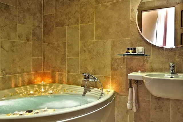 Eine mit Wasser gefüllte Eckbadewanne, umgeben von brennenden Kerzen.