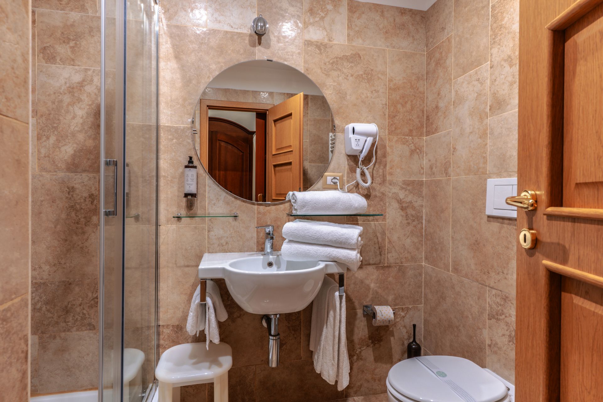 Badezimmer mit beigefarbenen Fliesenwänden, Waschbecken, Toilette, Spiegel und Dusche.