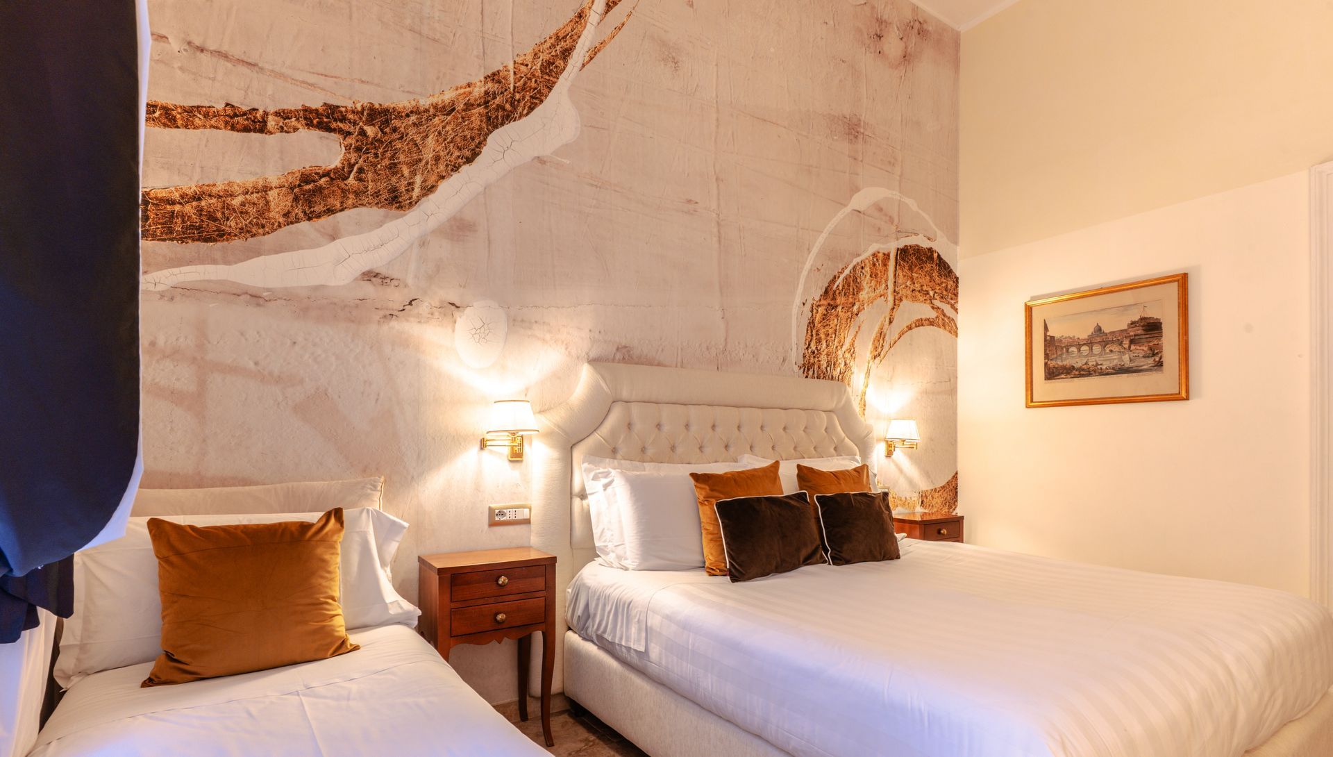 Hotelzimmer mit drei Betten, gemusterter Wand, Nachttisch, gerahmten Bildern und Lampen.