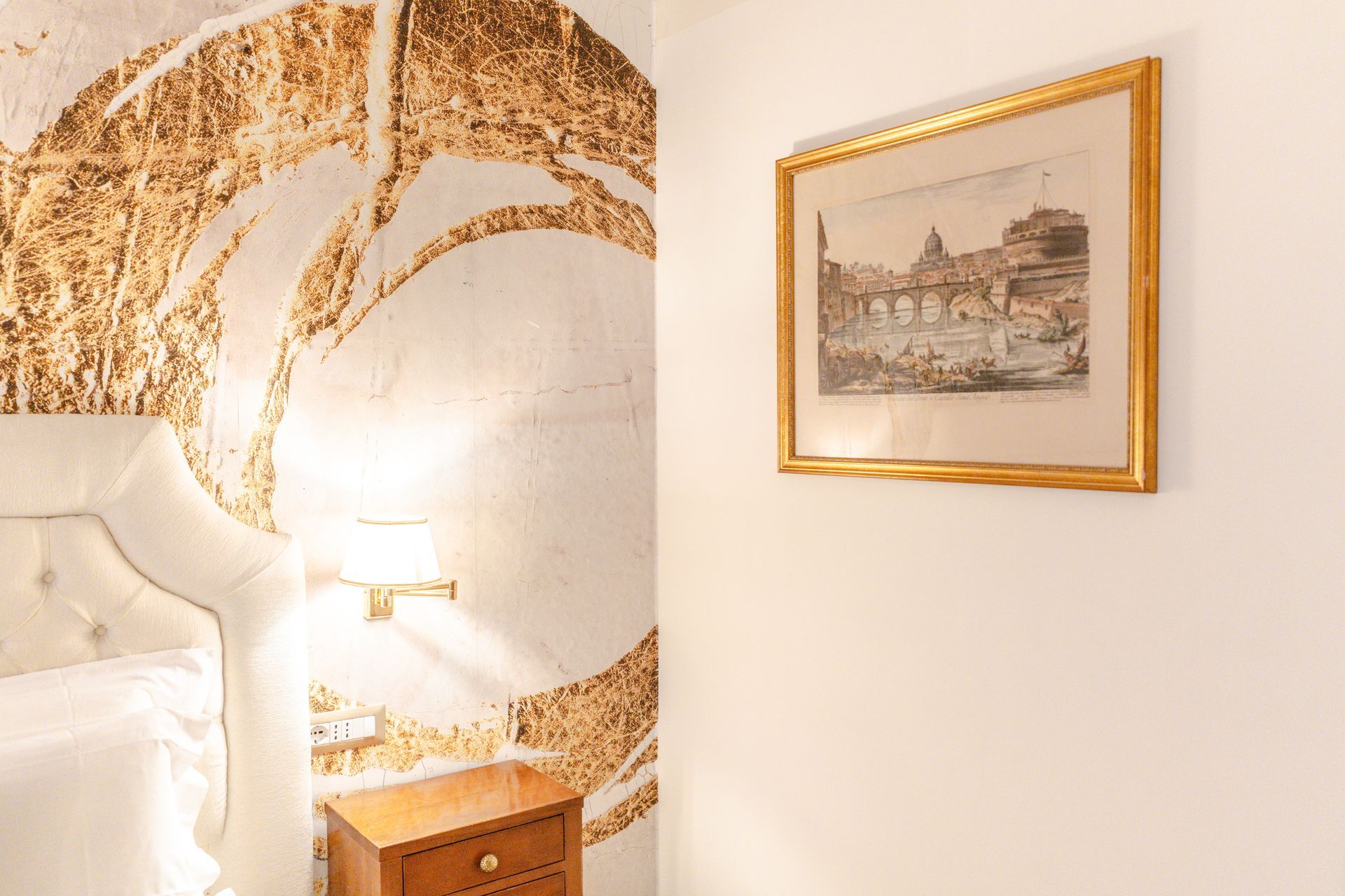 Schlafzimmer mit Kunstwerken an der weißen Wand und gemusterter Wand hinter dem Bett.