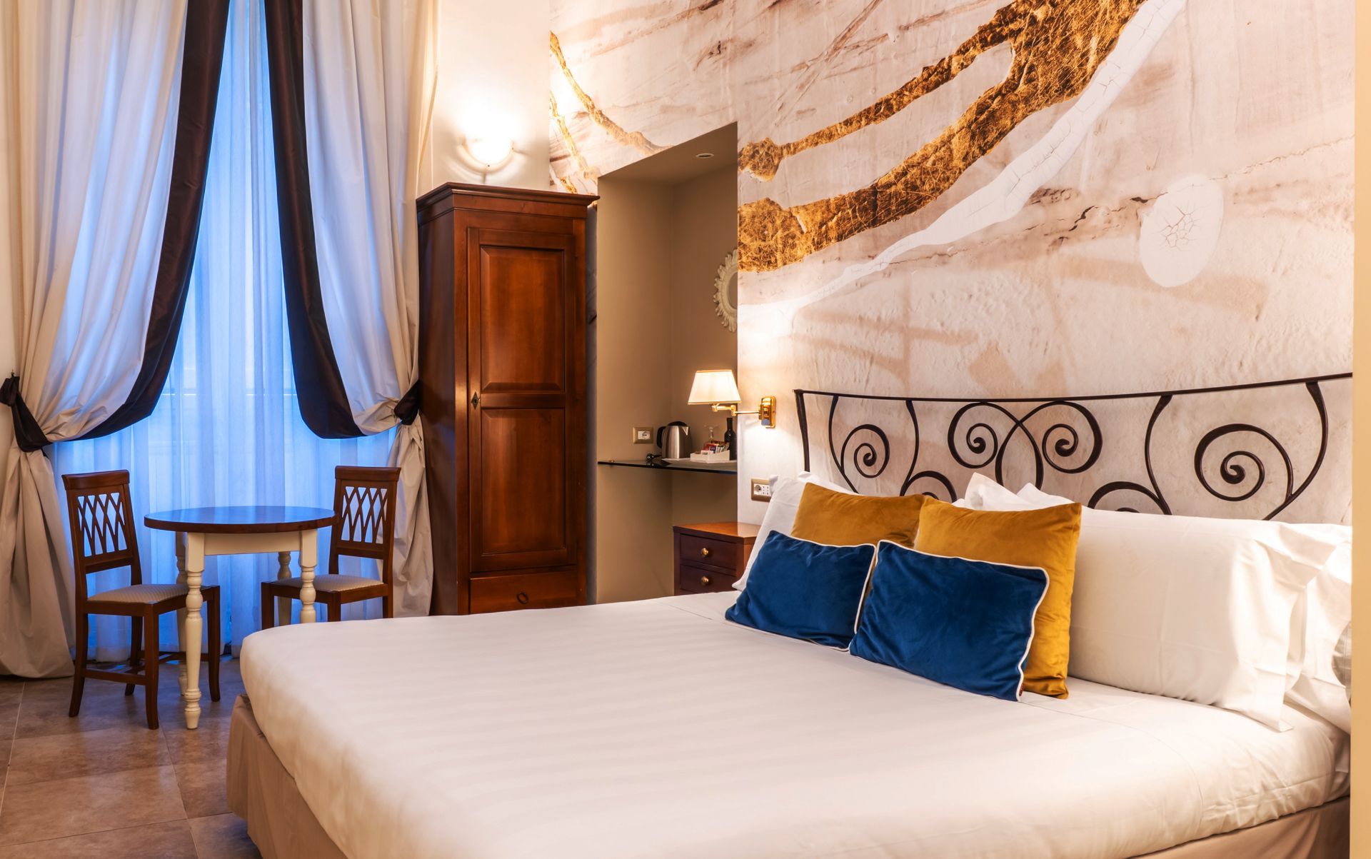 Hotelzimmer mit Bett, Tisch und Stühlen, einem großen Fenster mit Vorhängen und einem Holzschrank.