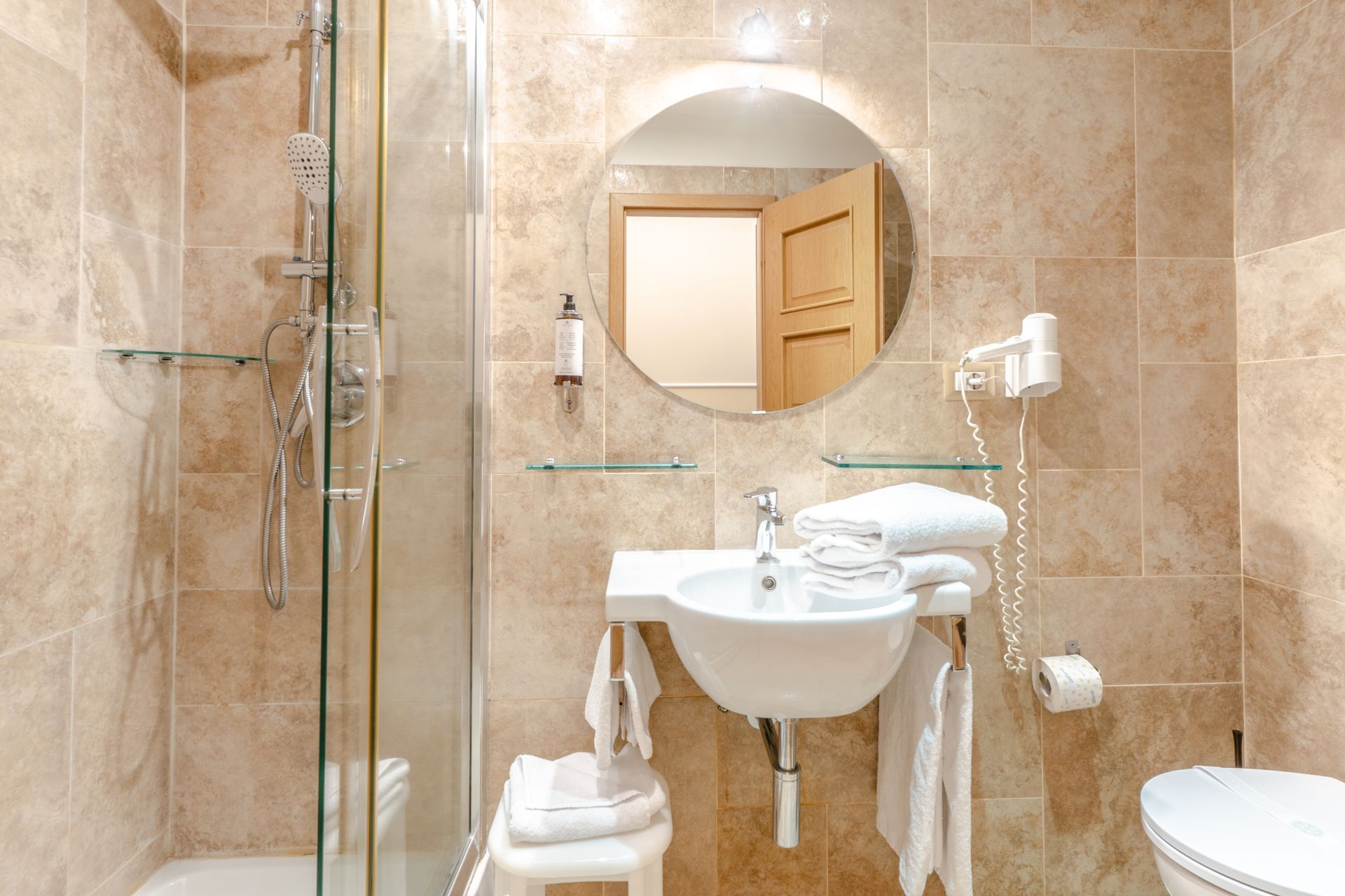 Kleines Badezimmer mit Dusche, Waschbecken, Spiegel und Toilette. Beige geflieste Wände.