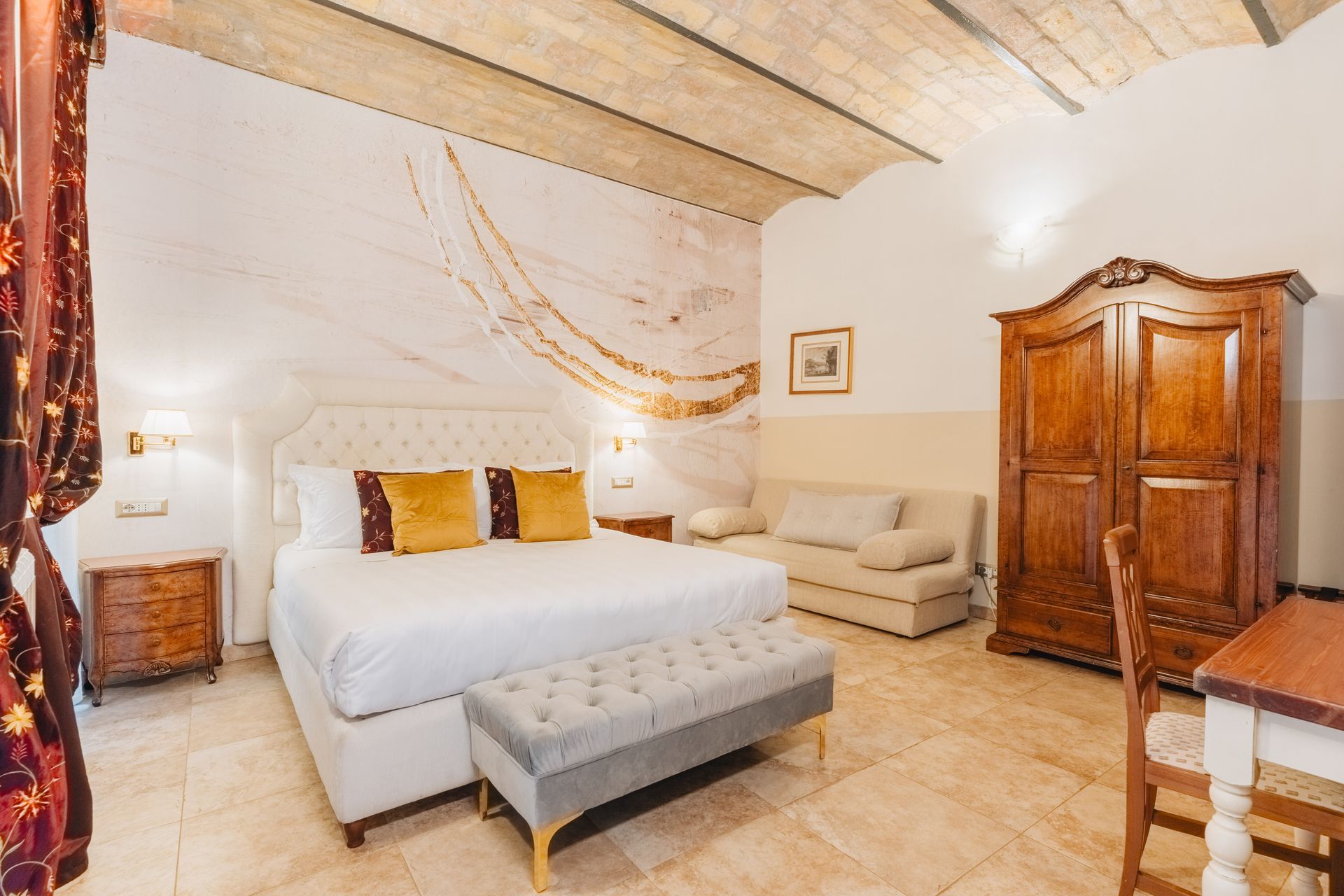 Hotelzimmer mit großem Bett, Sofa, Holzschrank und Schreibtisch. Die Wände sind weiß und der Boden ist gefliest.