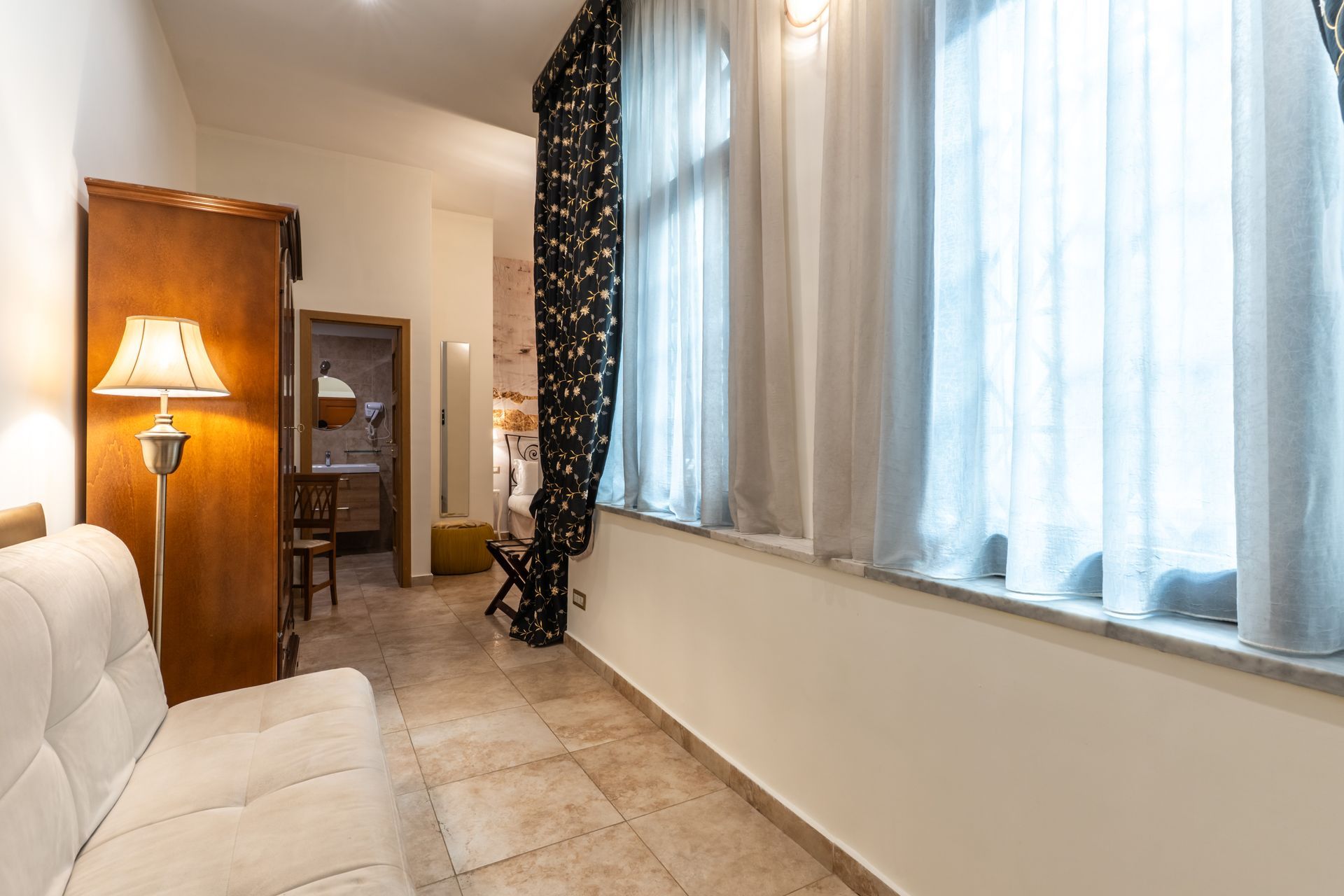 Ein kleiner Wohnungsflur mit einem Sofa, hohen Fenstern und einer Tür, die zu einem Badezimmer führt.