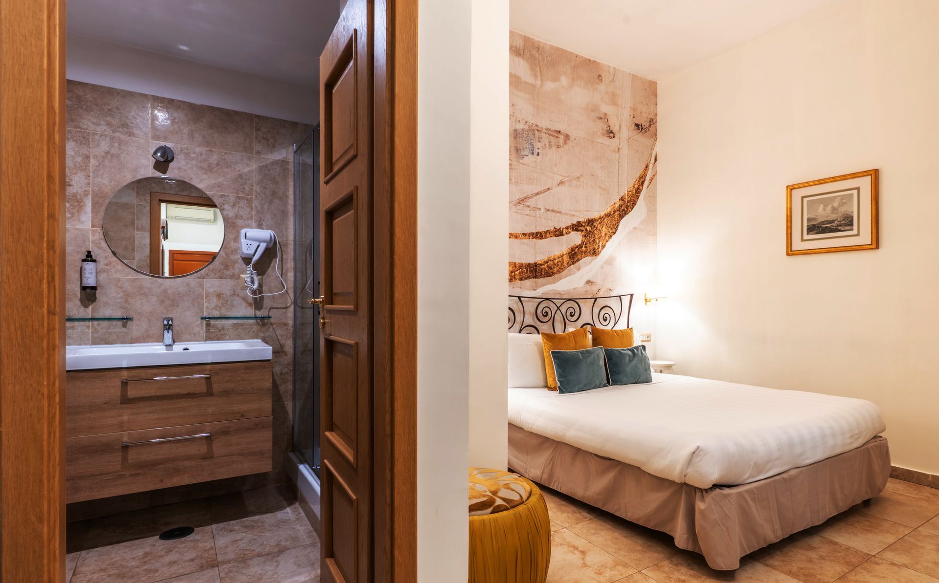 Hotelzimmer-Interieur: offene Tür zum Badezimmer mit Waschbecken und Schlafzimmer mit Bett und Kunstwerken.