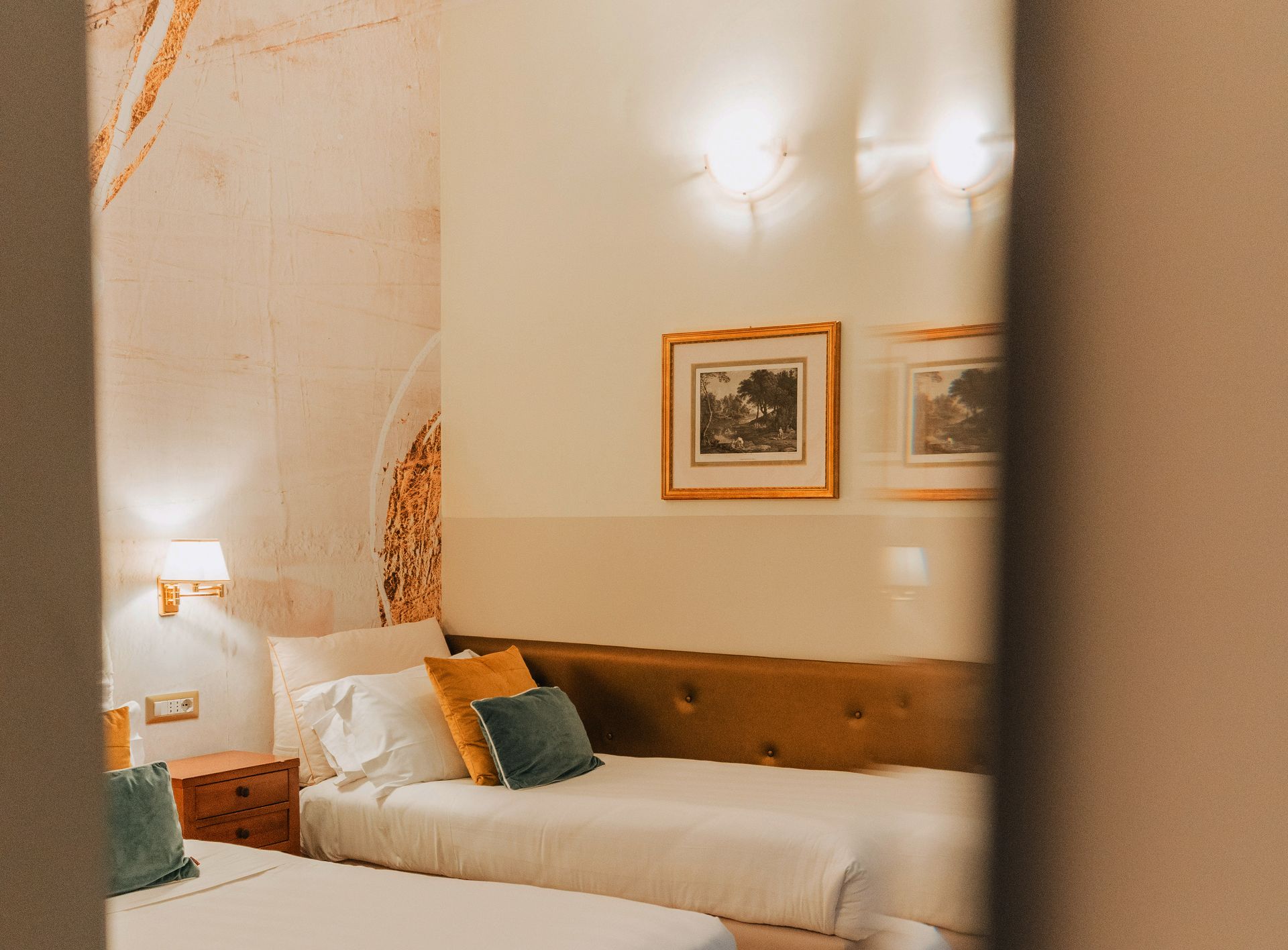 Zwei Einzelbetten in einem neutral gehaltenen Hotelzimmer mit Kunstwerken und einem Kopfteil, gesehen von einer Tür aus.