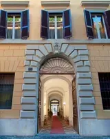 Fassade eines Gebäudes mit gewölbtem Eingang und mehreren Fenstern mit Fensterläden; beige und steinfarben.