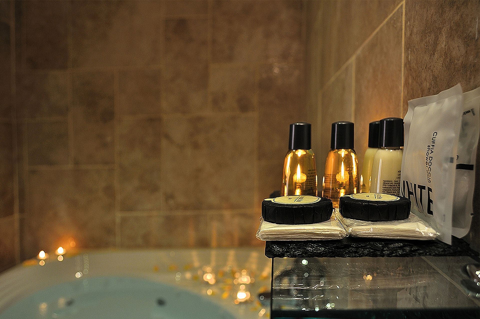 Badezimmerszene mit Kerzen, Toilettenartikeln auf einem Regal und einer Whirlpool-Badewanne mit kleinen Lichtern.