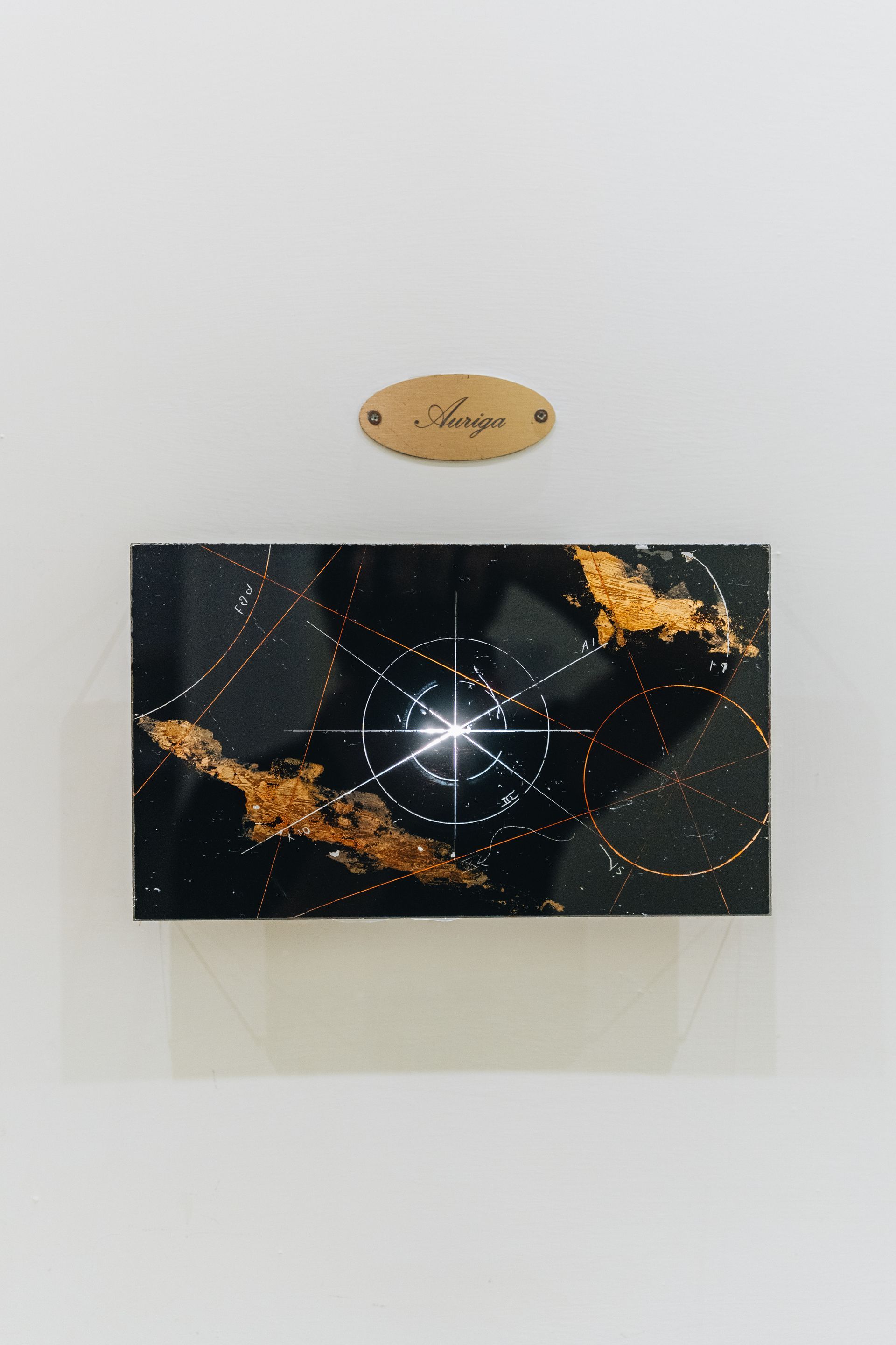 Abstrakte Kunst in Schwarz und Gold auf weißer Wand; darüber eine Holztafel mit der Aufschrift „Seraja“.