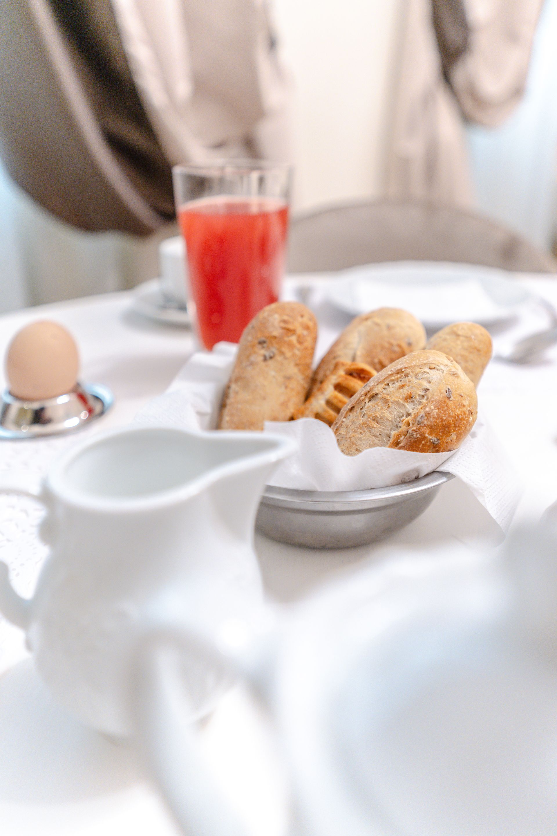 Frühstückstisch: Brotkorb mit Brötchen, Saft, Ei, weiße Tischdecke.