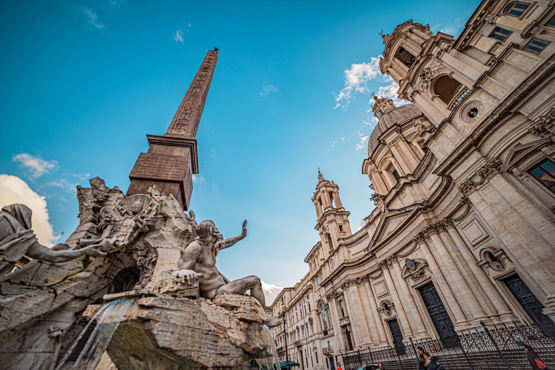 Vierströmebrunnen mit Skulptur und Obelisk auf der Piazza Navona in Rom. Blauer Himmel, weißes Gebäude.