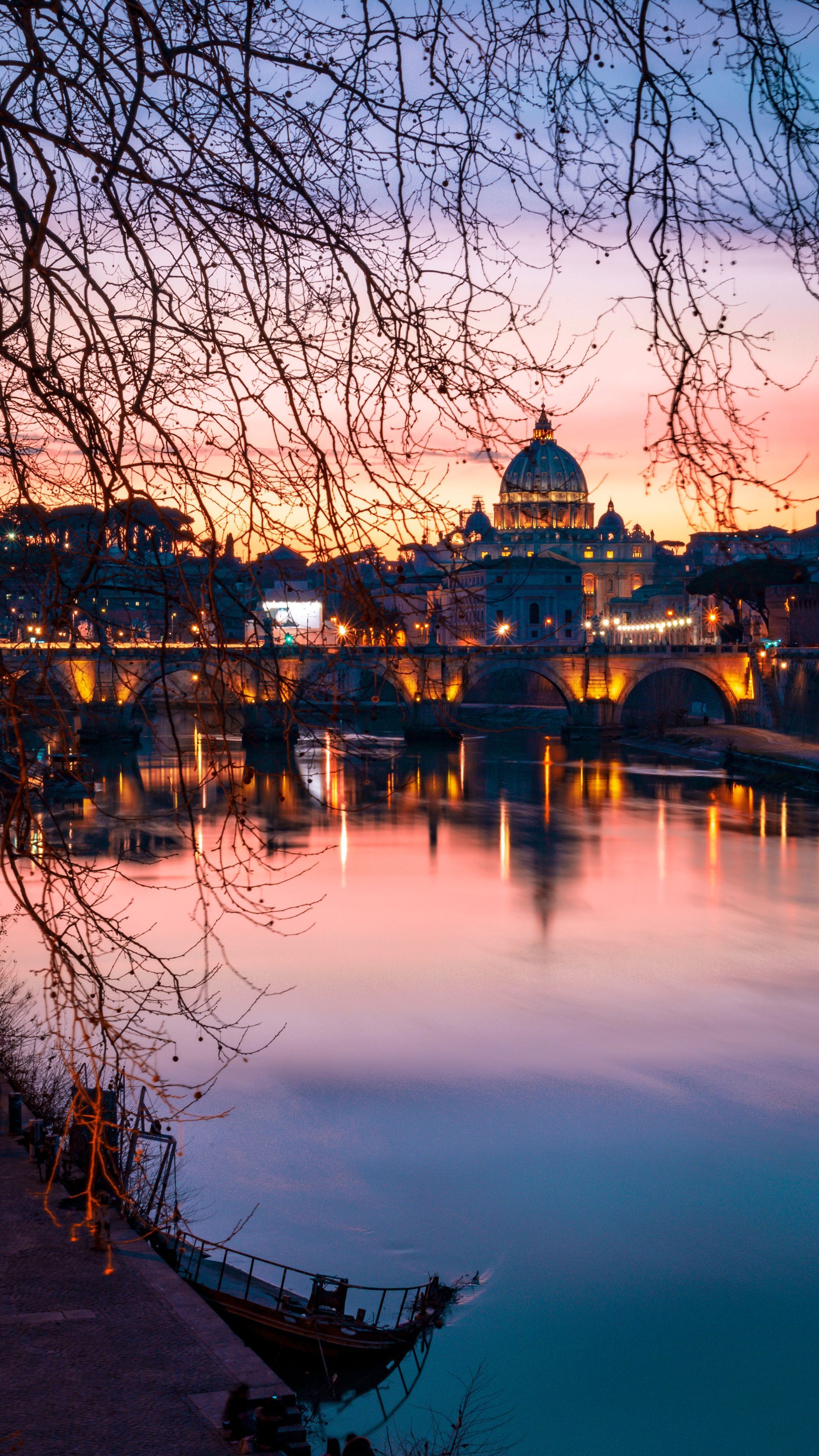 Sonnenuntergang über dem Tiber in Rom, mit dem Petersdom in der Ferne, der sich im Wasser spiegelt.