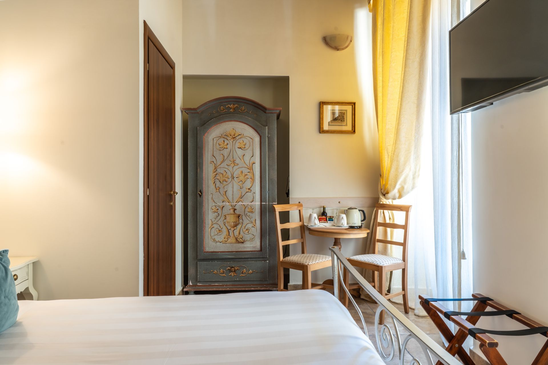 Schlafzimmer mit reich verziertem Kleiderschrank, kleinem Tisch, Stühlen und Fernseher.