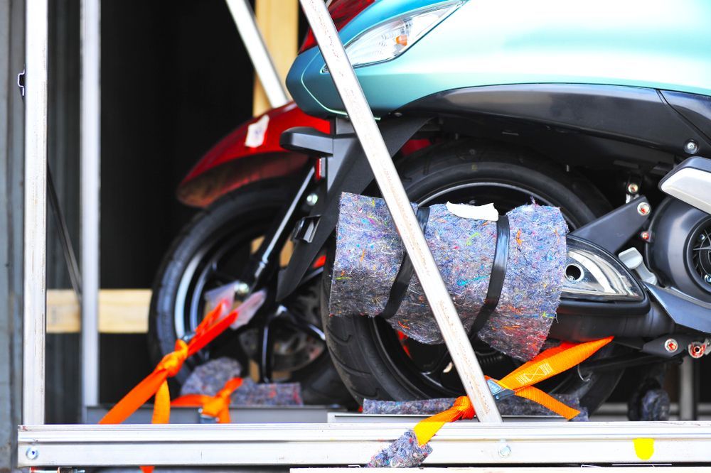 A turquoise and a red scooter are secured with orange straps inside a trailer for transport.