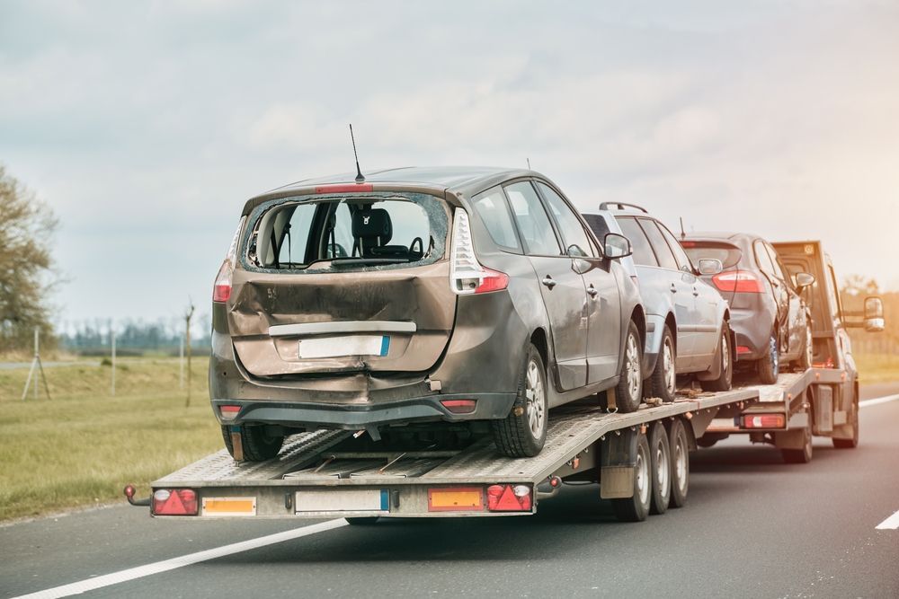 A car carrier truck transports several damaged vehicles on a highway.