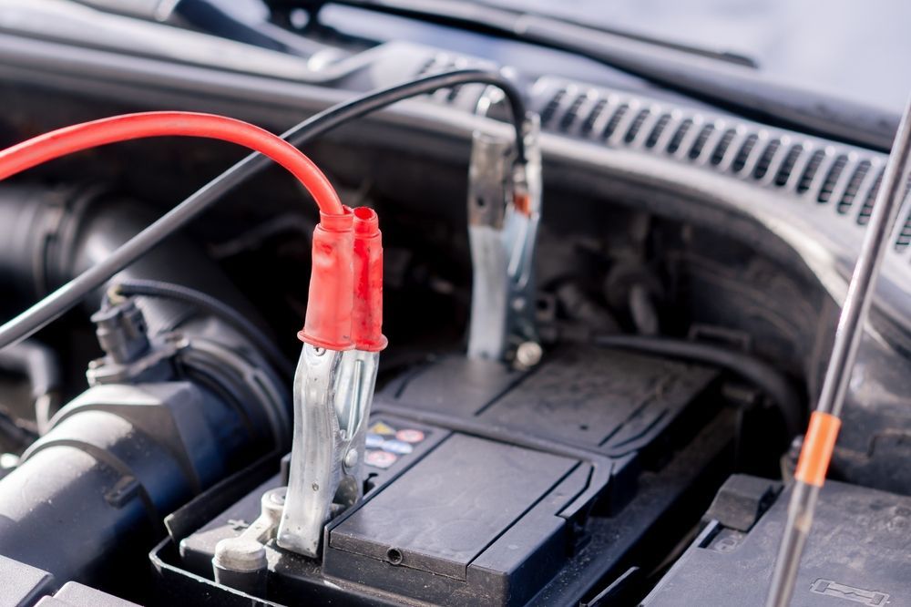 Jumper cables attached to a car battery under the hood of a vehicle.