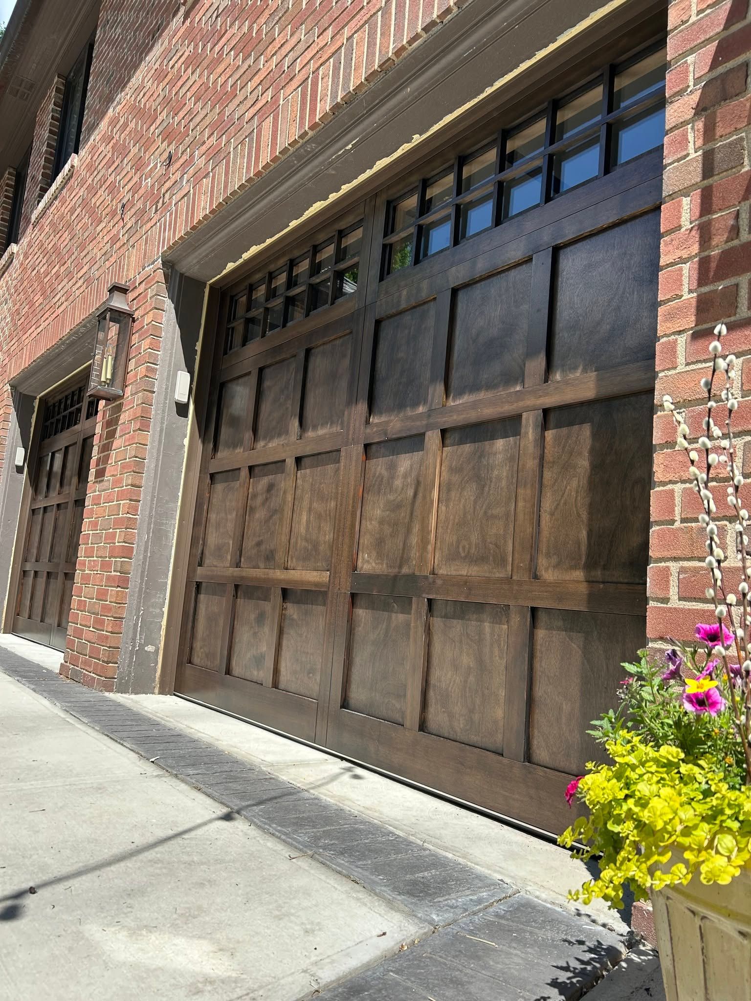 Brick building with a large dark wooden garage door and a small flower planter beside the sidewalk.