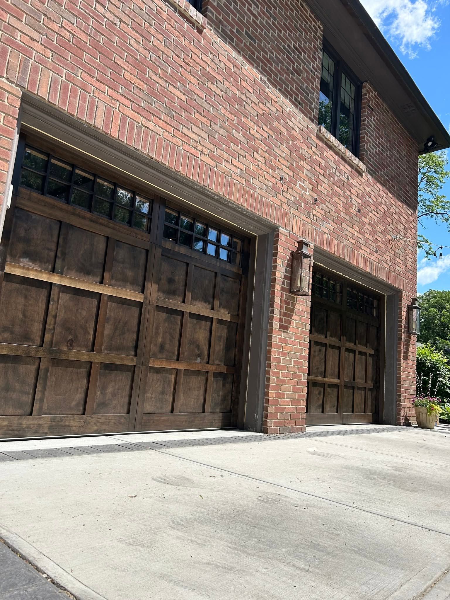 Brick house exterior with dark wooden garage doors and sloped concrete driveway