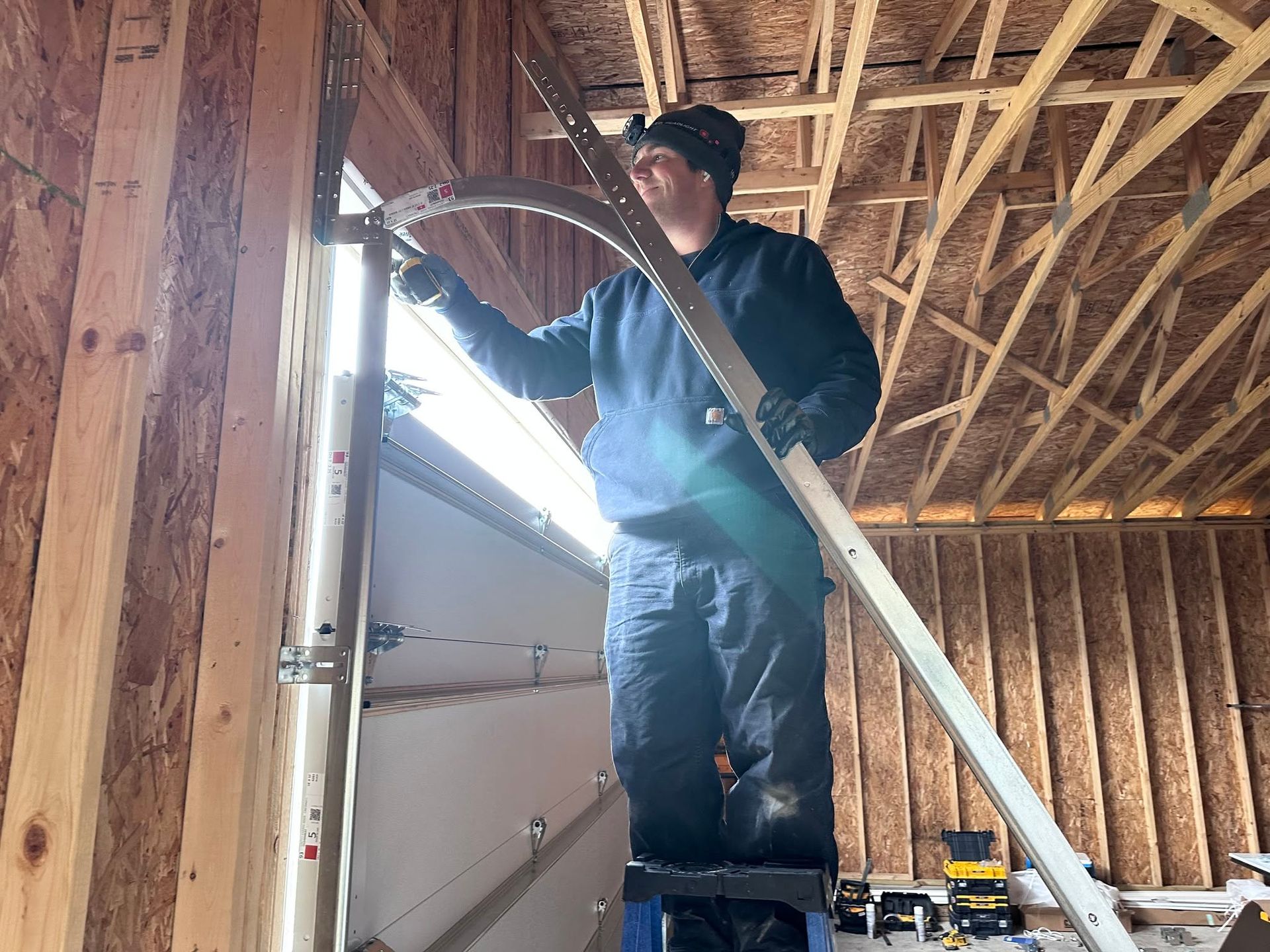 Worker standing on a ladder inside an unfinished wooden building, inspecting framing near a doorway.
