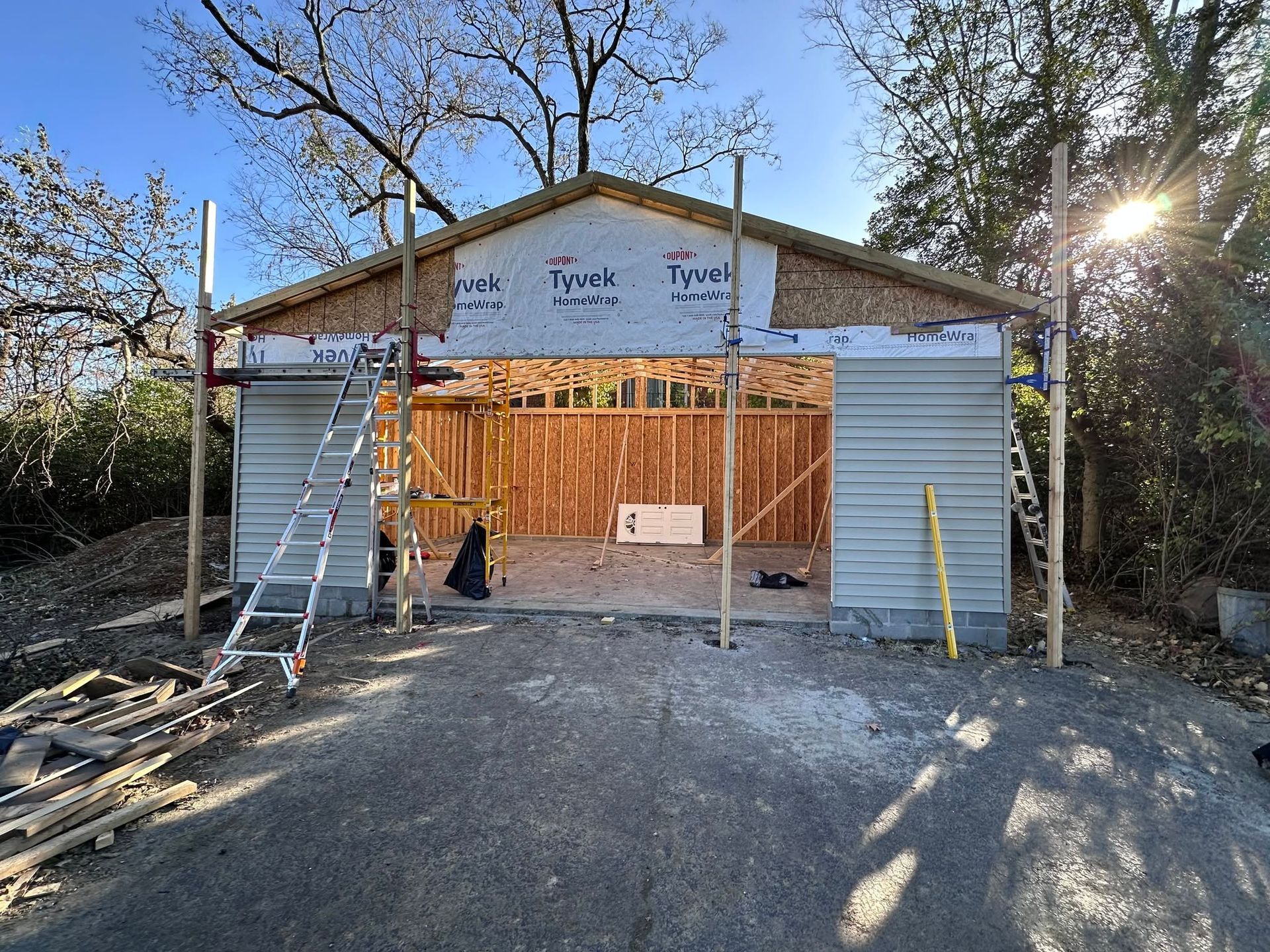 Partially built house framed in wood with white siding, gravel driveway, and construction materials outside