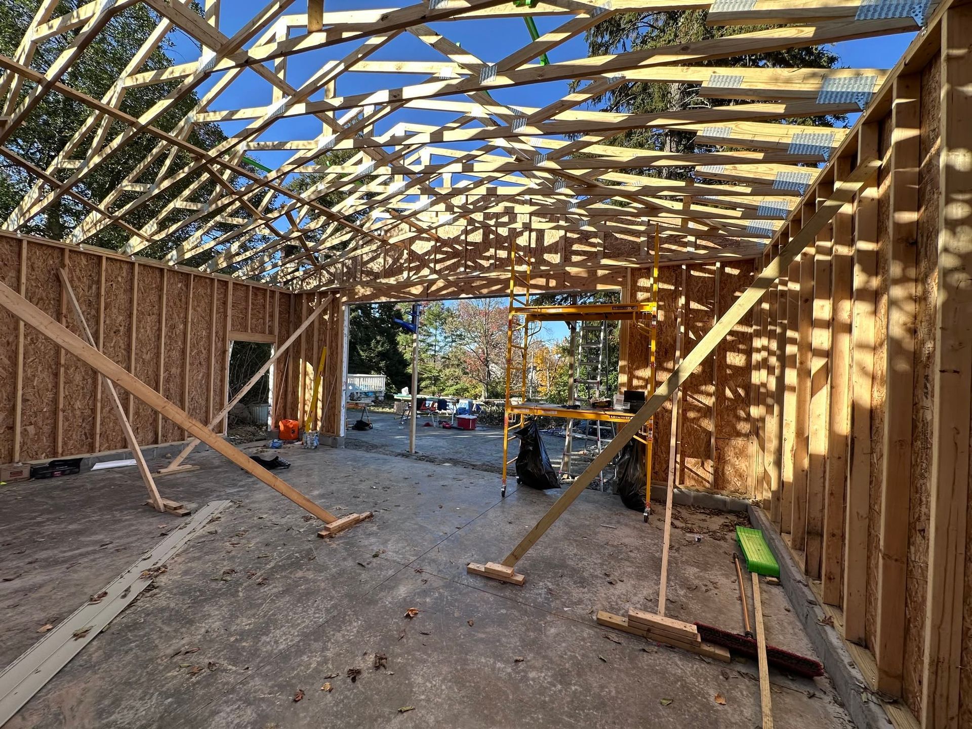 Interior of a house under construction with exposed wooden framing and roof trusses, tools on the floor.