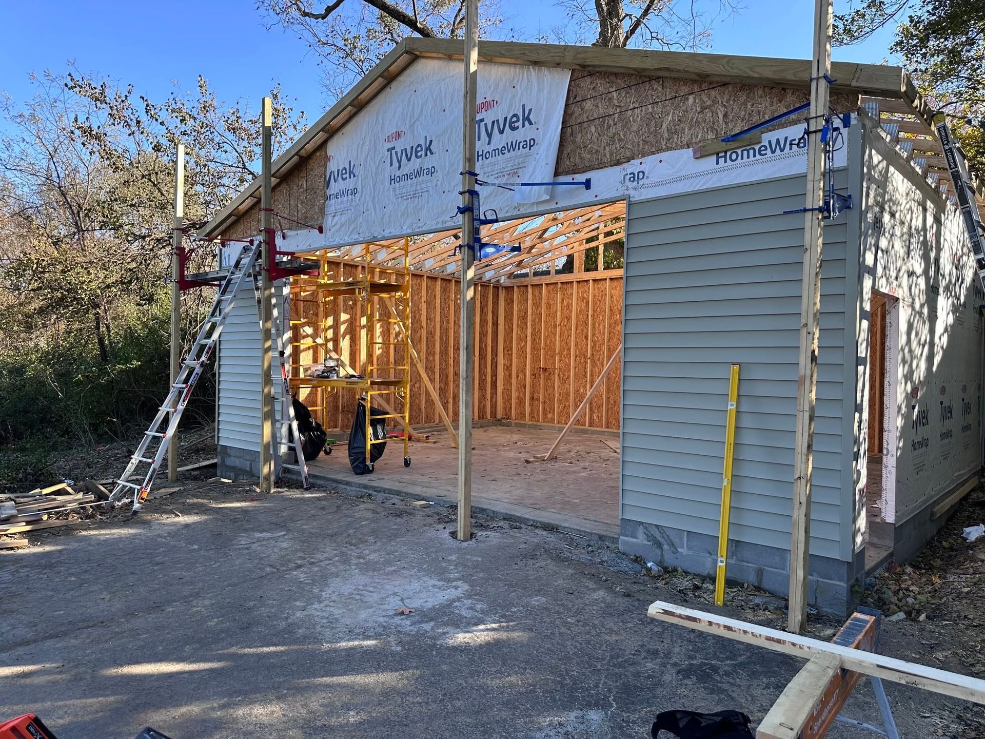 Partially built house framed in wood, with gray siding, scaffolding, and roof under construction