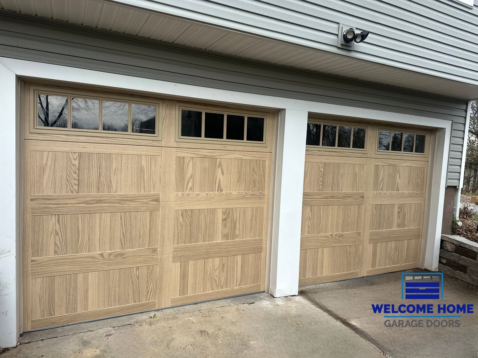 Two wood-paneled garage doors on a house with small upper windows under gray siding.