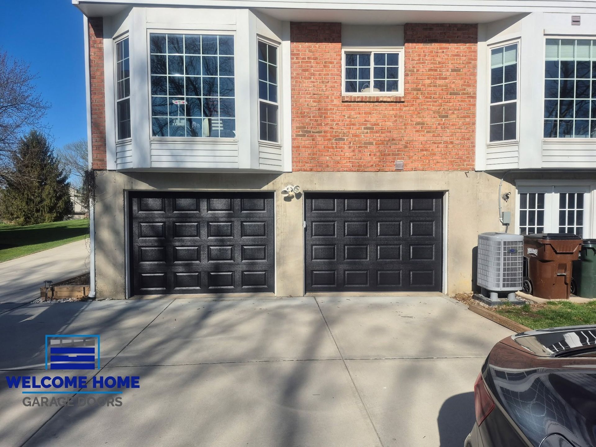 Front view of a townhouse with two black garage doors and a brick-and-white exterior on a sunny day