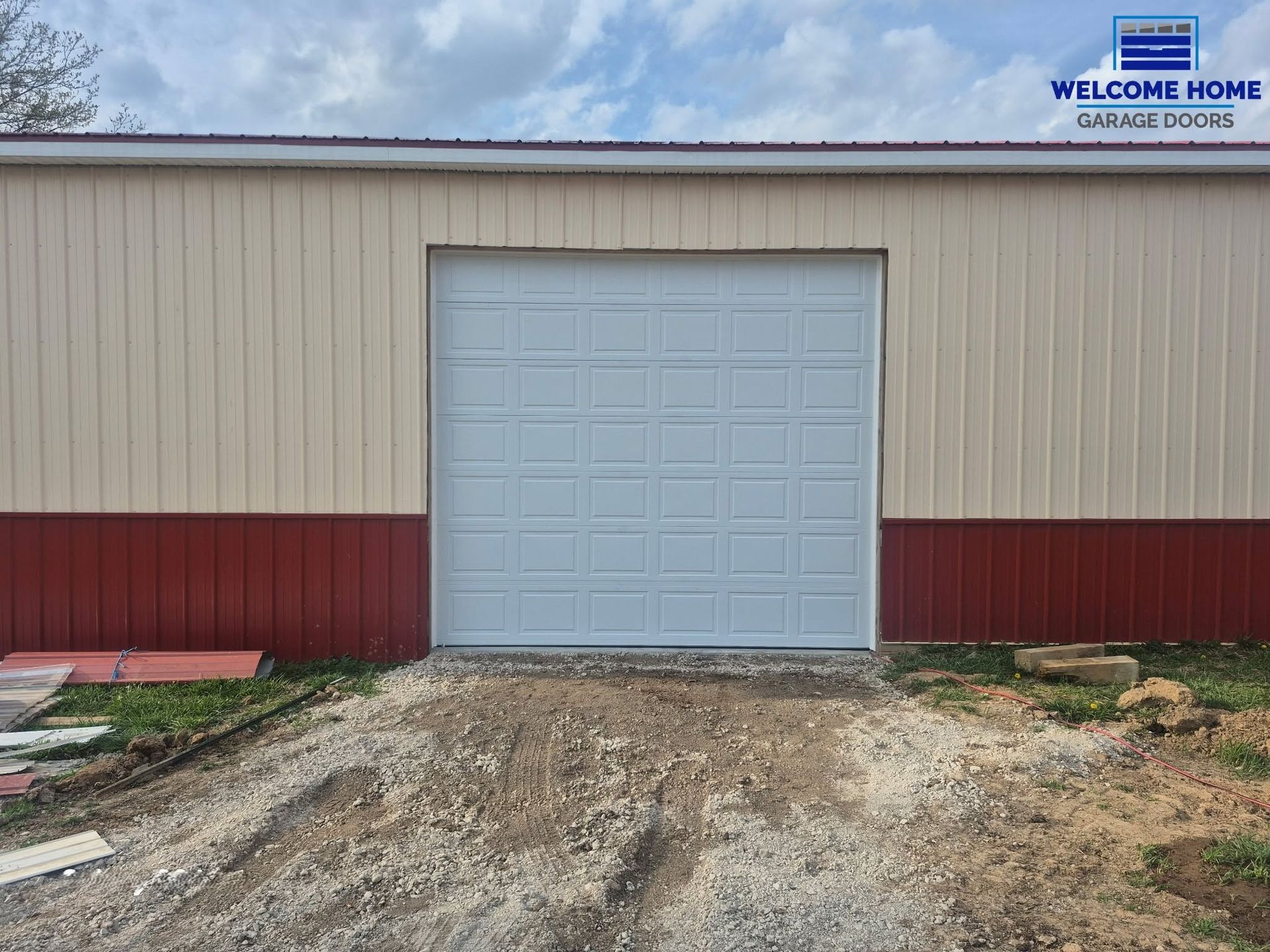 Warehouse building with a light blue roll-up door and red trim, viewed from a dirt driveway.
