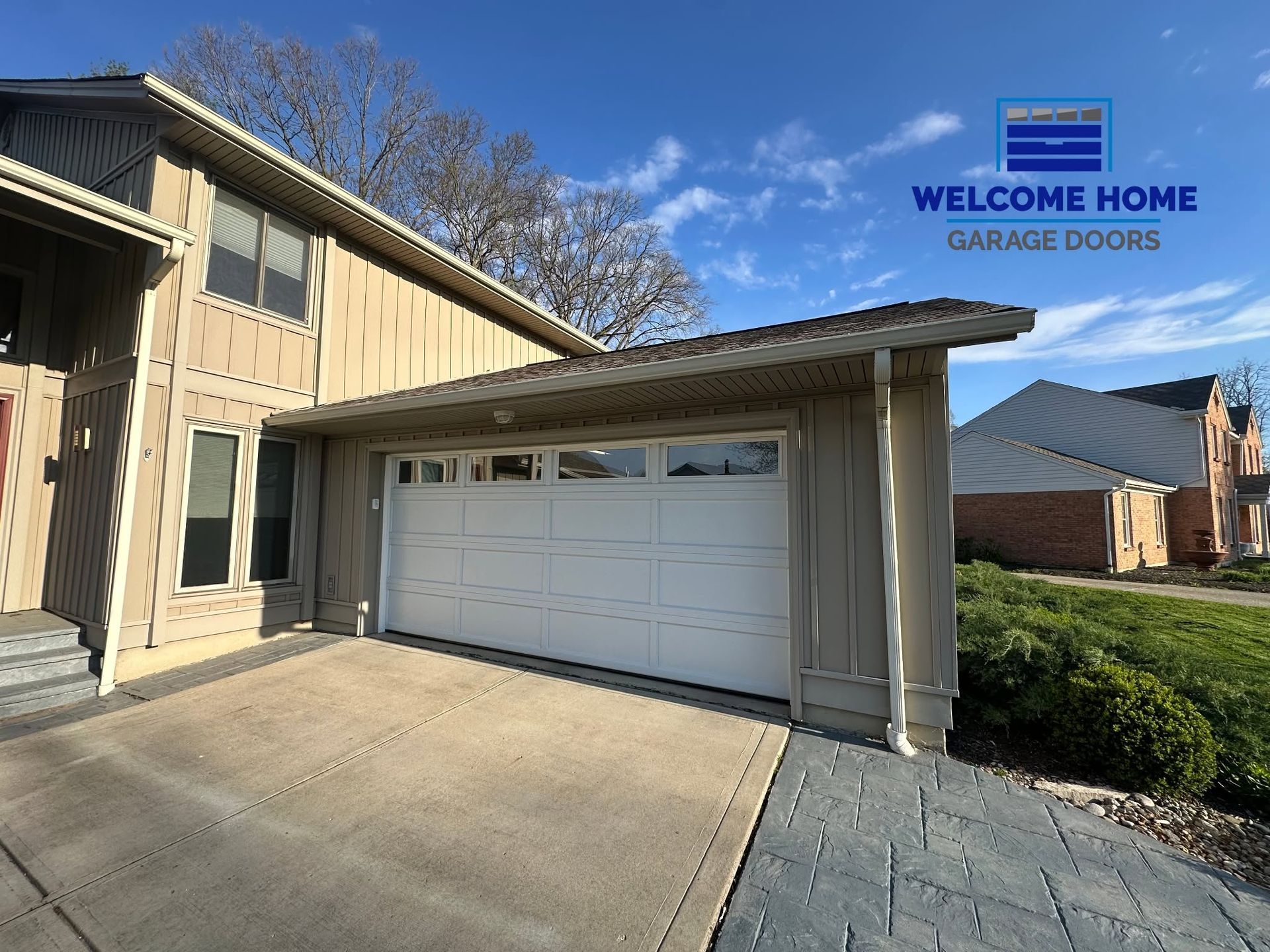 Suburban home exterior with beige siding and a white double garage door under a clear blue sky