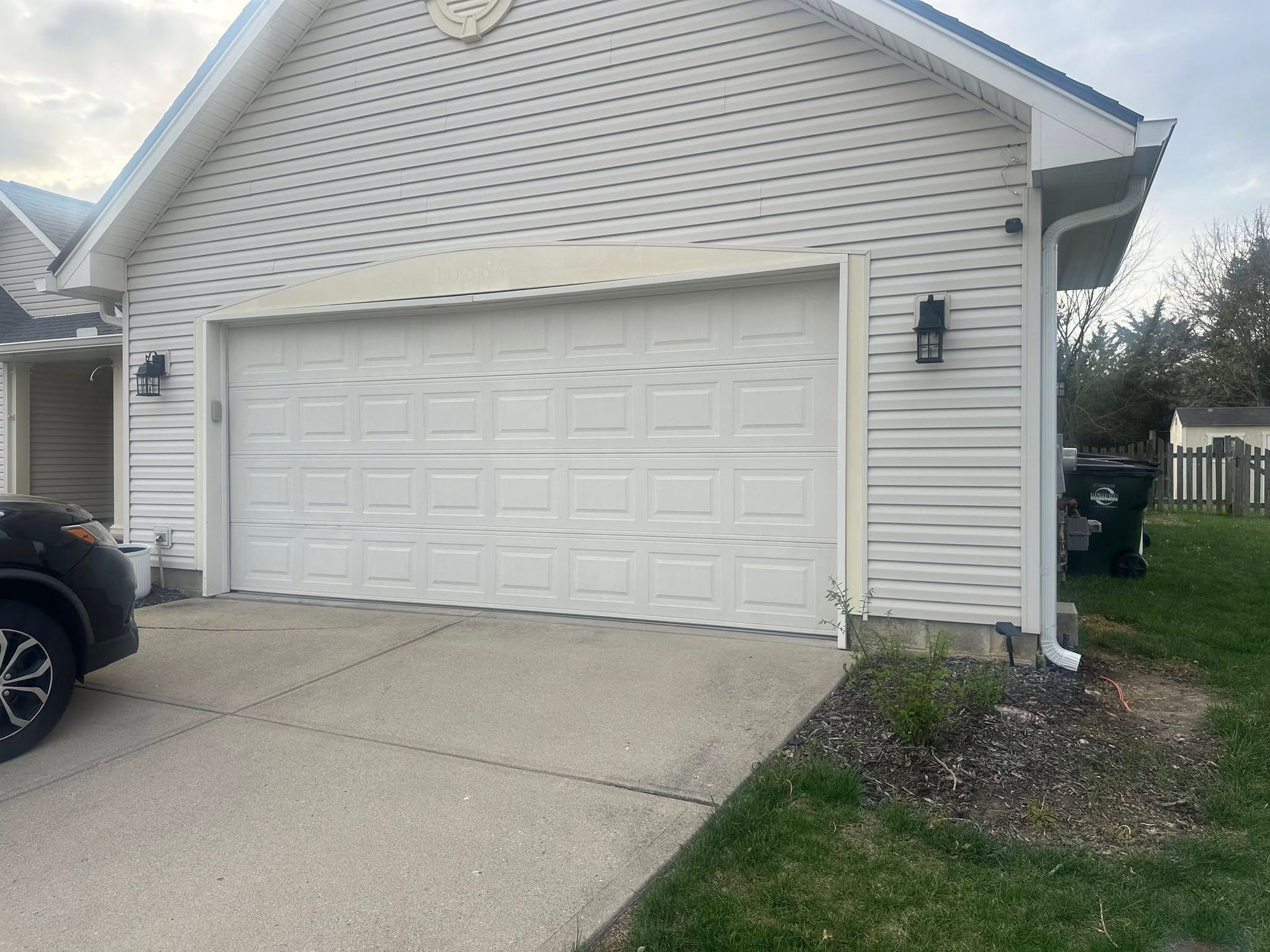 White two-car garage with driveway, beige siding, and black wall lanterns