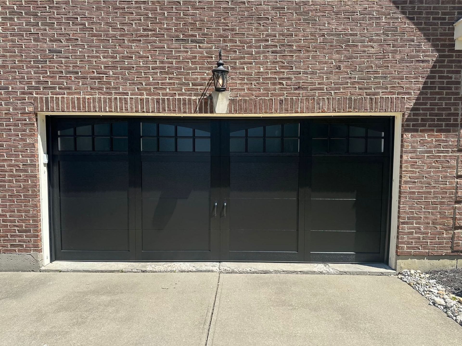 Dark glass garage door set in a brick building wall, viewed from a concrete driveway.