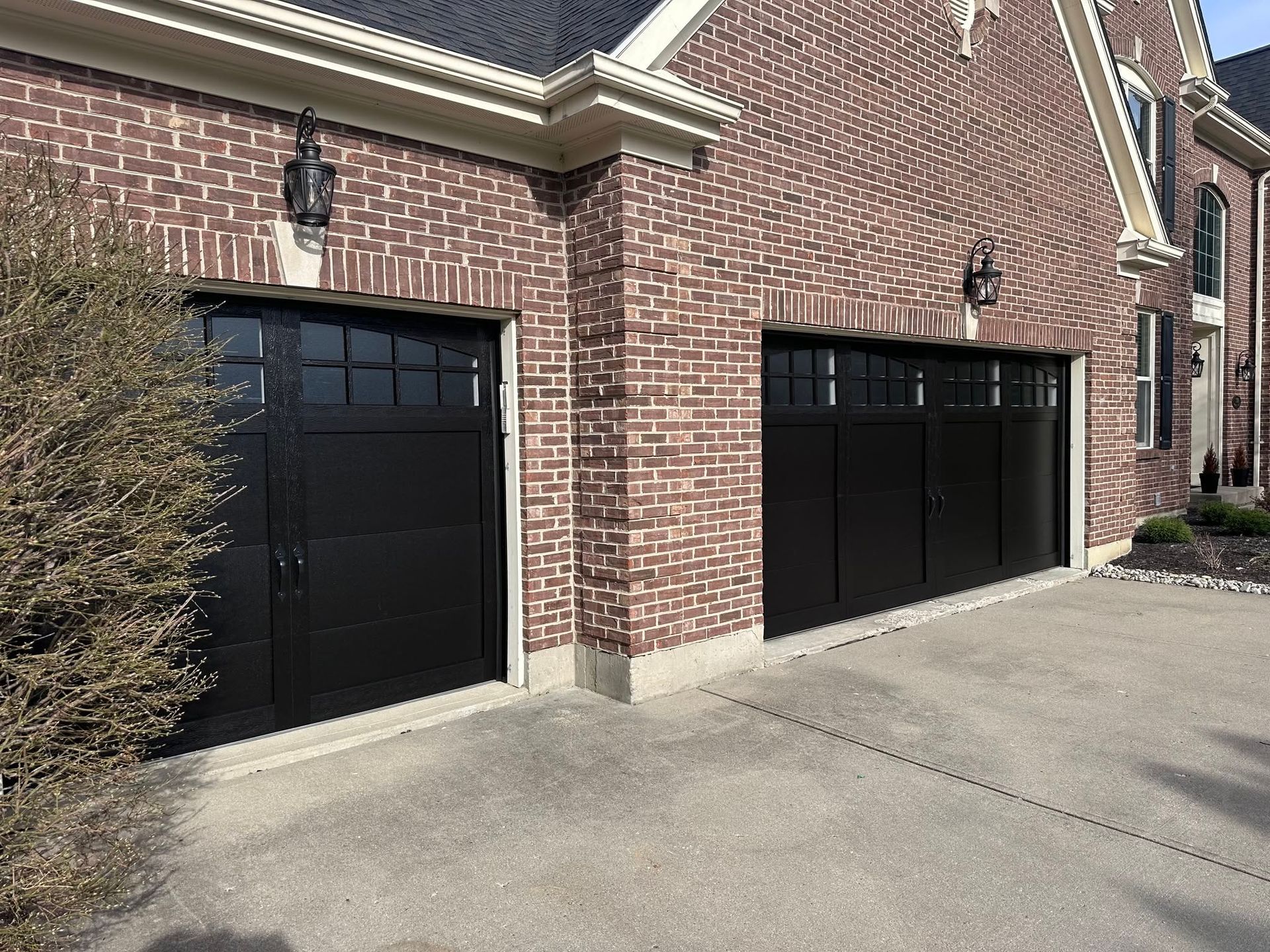 Two black garage doors on a brick house with a concrete driveway