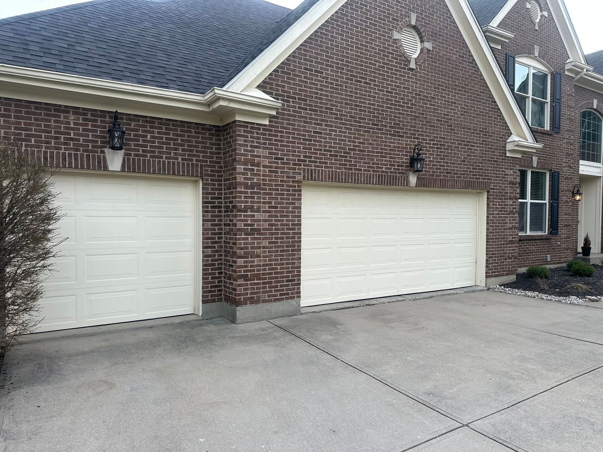Brick suburban house with two white garage doors and a concrete driveway