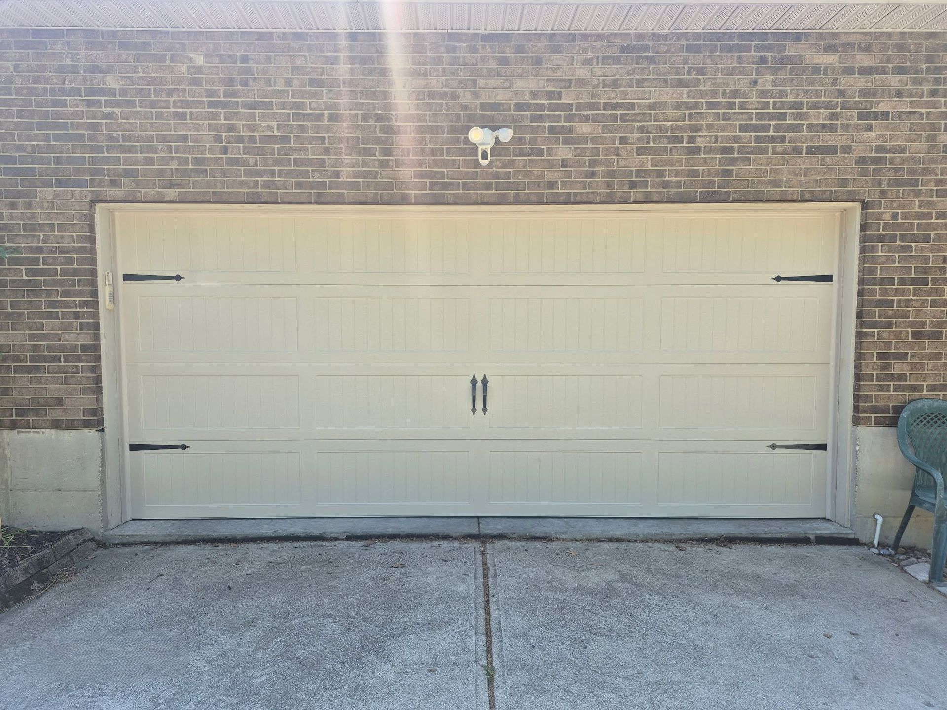 Beige double garage door set in a brick wall with concrete driveway in front.