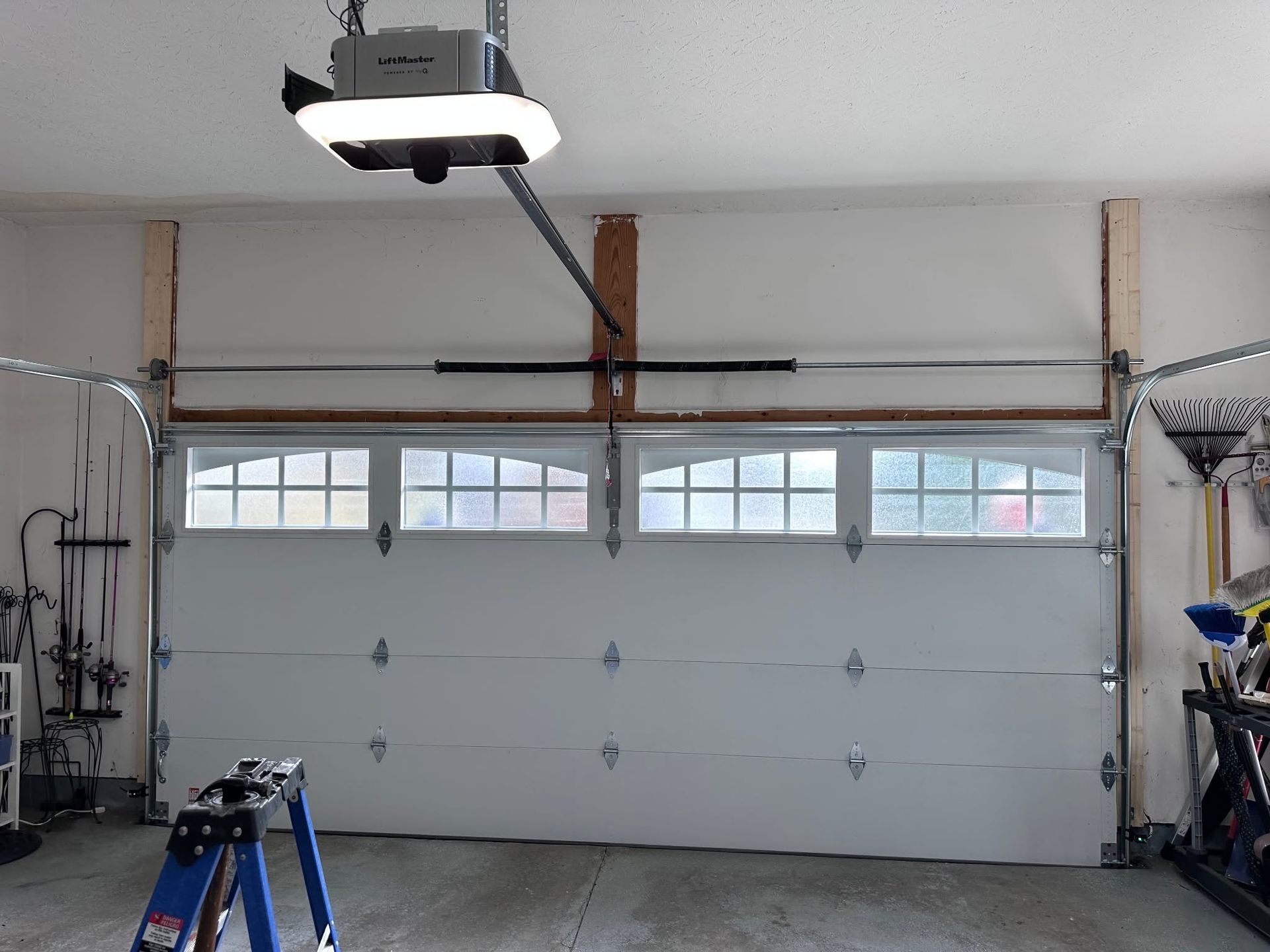 Garage interior with closed white sectional door, ceiling opener, and tools along the sides.