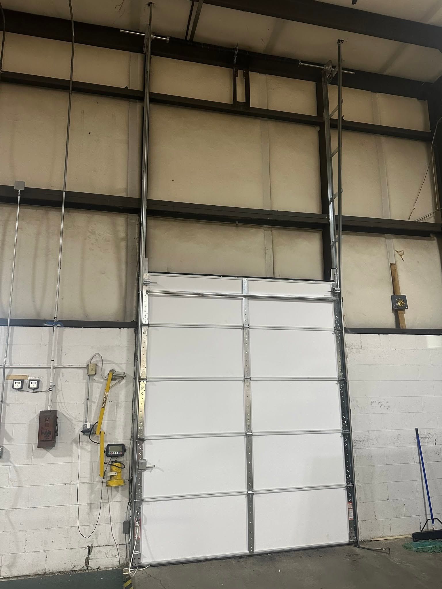 Interior warehouse wall with a large white roll-up door and exposed metal beams.