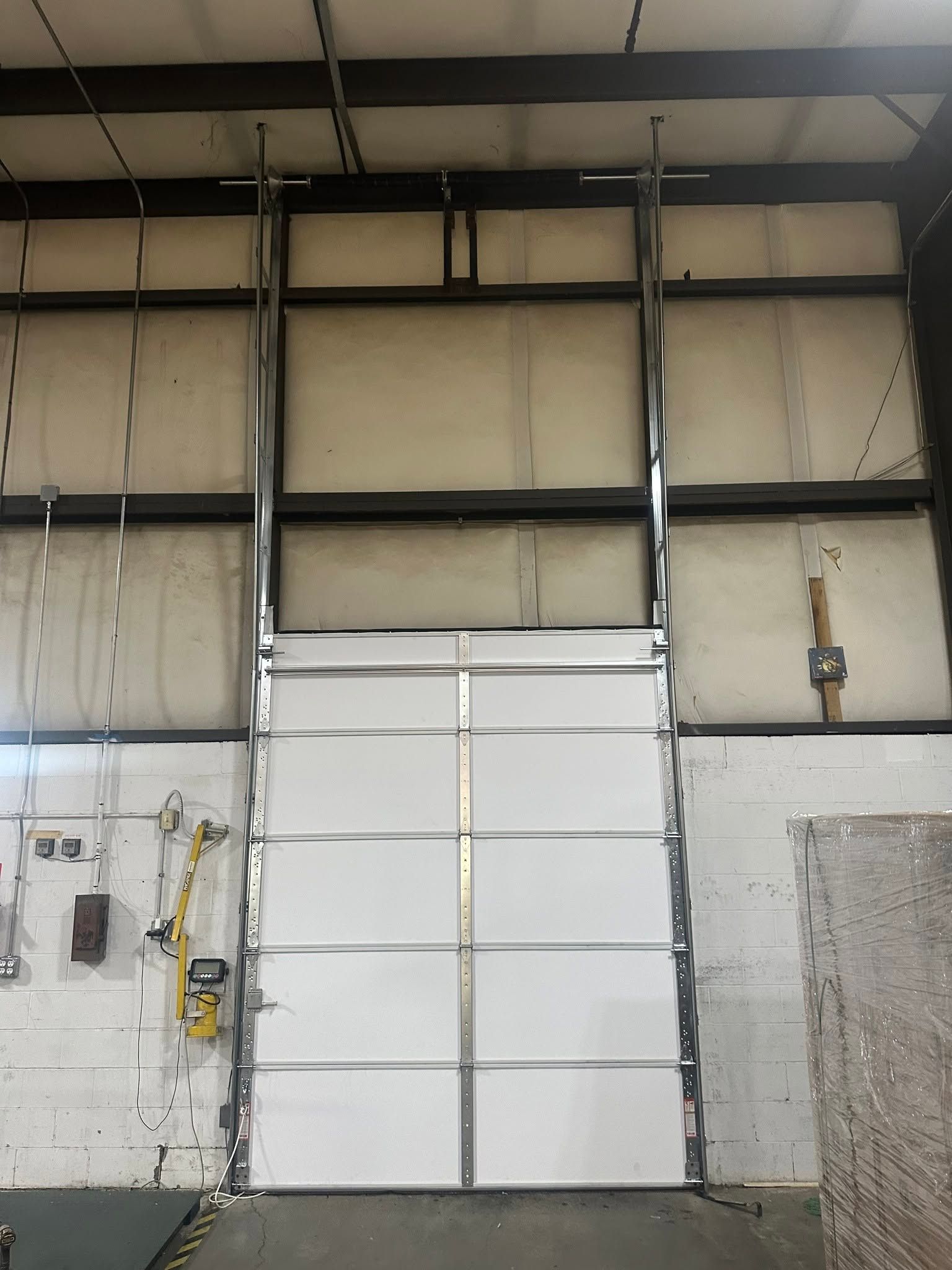 Large white industrial garage door in a warehouse interior with concrete walls and exposed beams