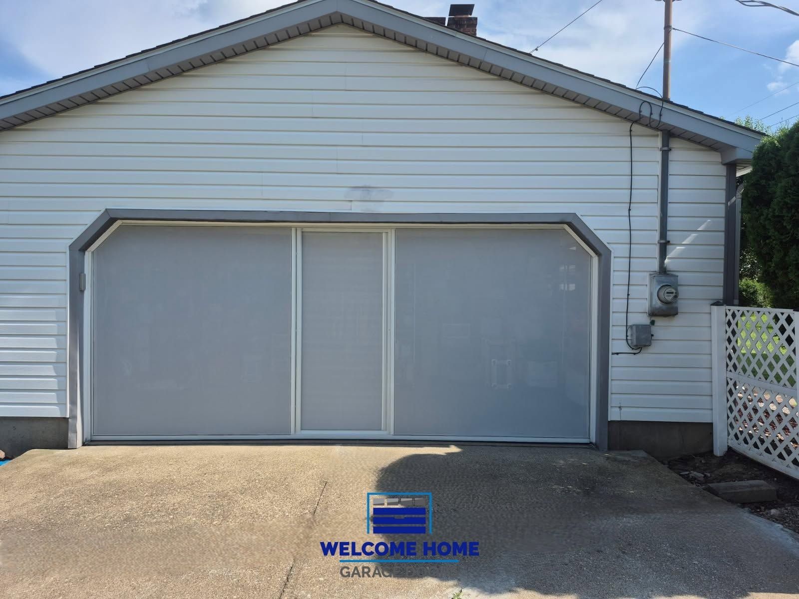 Detached white garage with two closed doors and a driveway, “Welcome Home” sign on the pavement