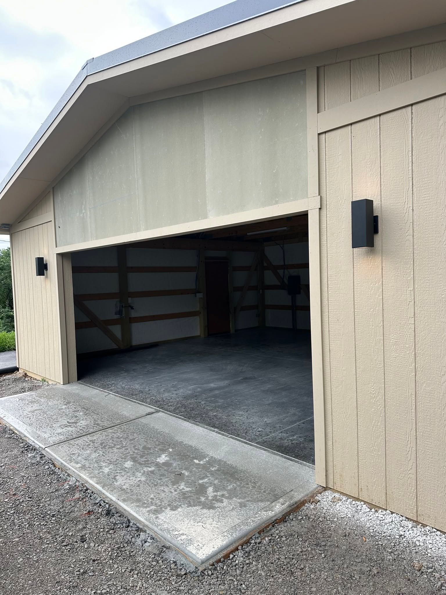 Open garage with gravel driveway and ramp leading inside a tan outbuilding