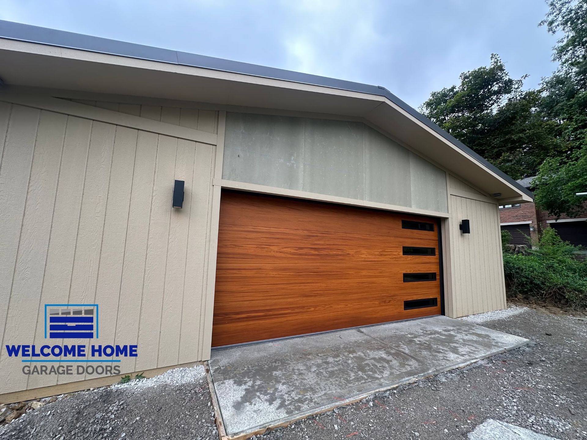 Modern garage with tan siding and a large wooden door, shown from the driveway.