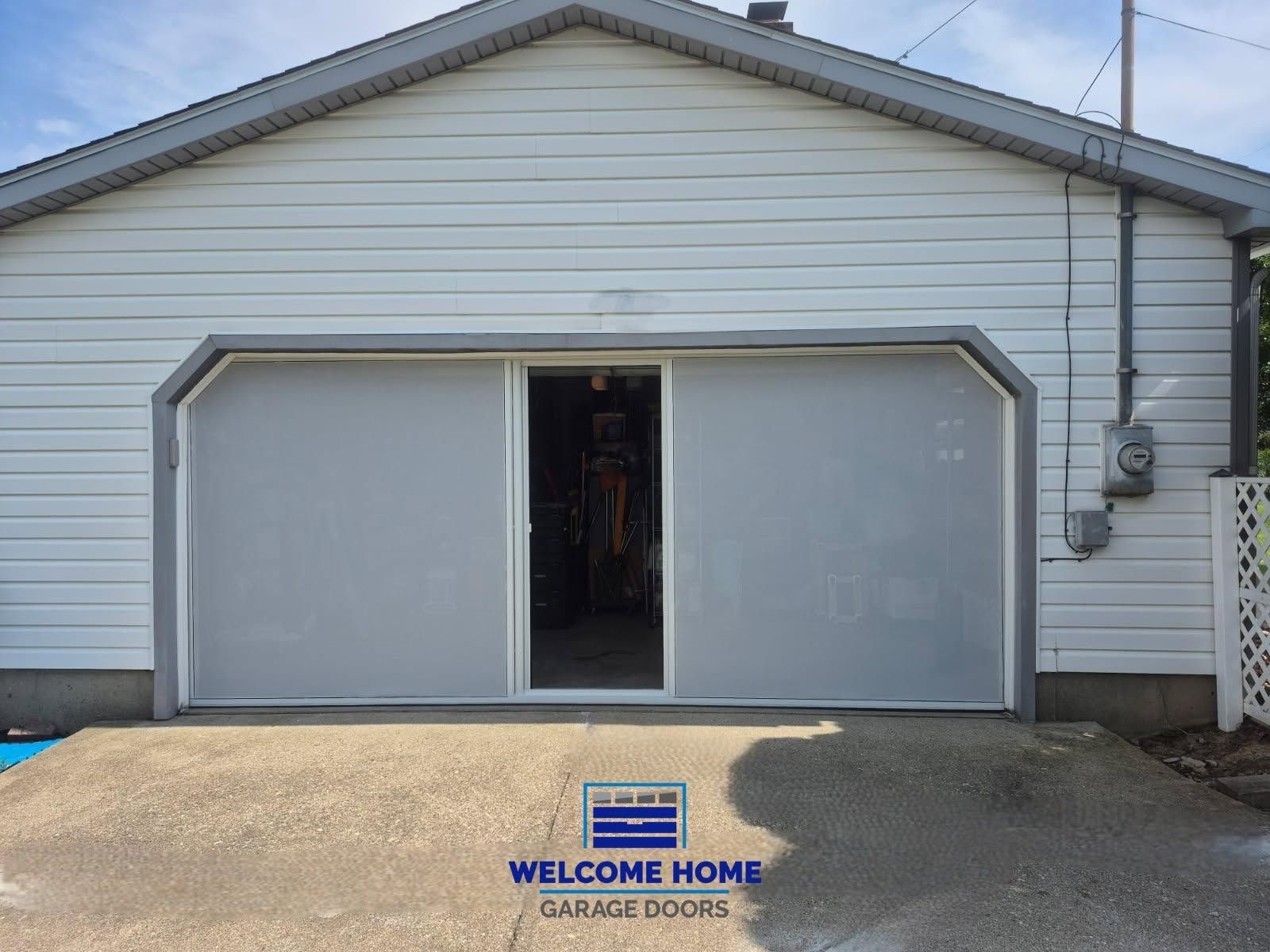 Front of a gray garage with an open door and a “WELCOME HOME” mat on the driveway.