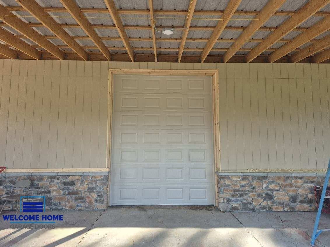 Front porch with a closed white door, stone base, tan siding, and exposed wooden roof beams