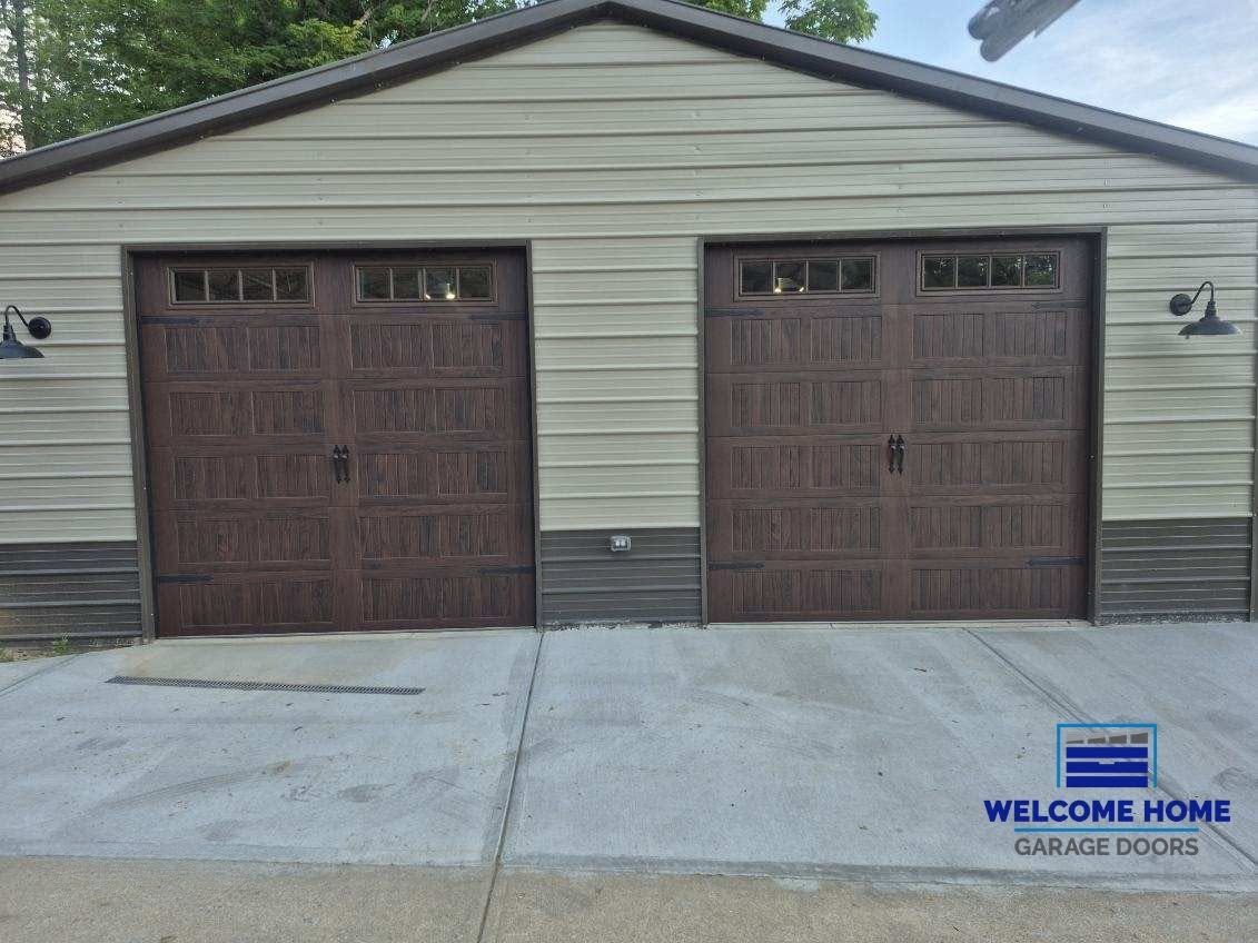 Detached double garage with brown doors, beige siding, and a welcome-home sign by the driveway