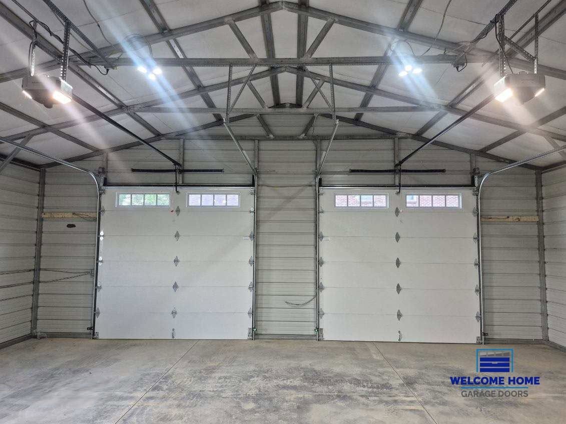 Empty metal warehouse interior with two large white roll-up doors and overhead lights