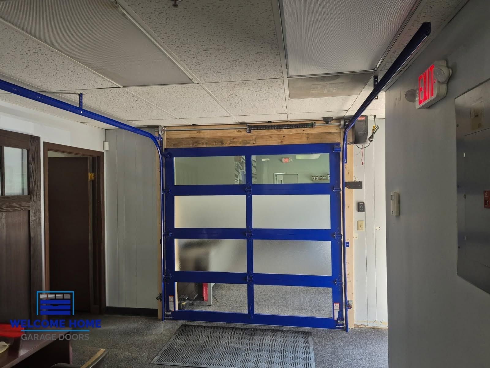 Indoor garage with a blue roll-up door covered in tape and plastic sheeting.