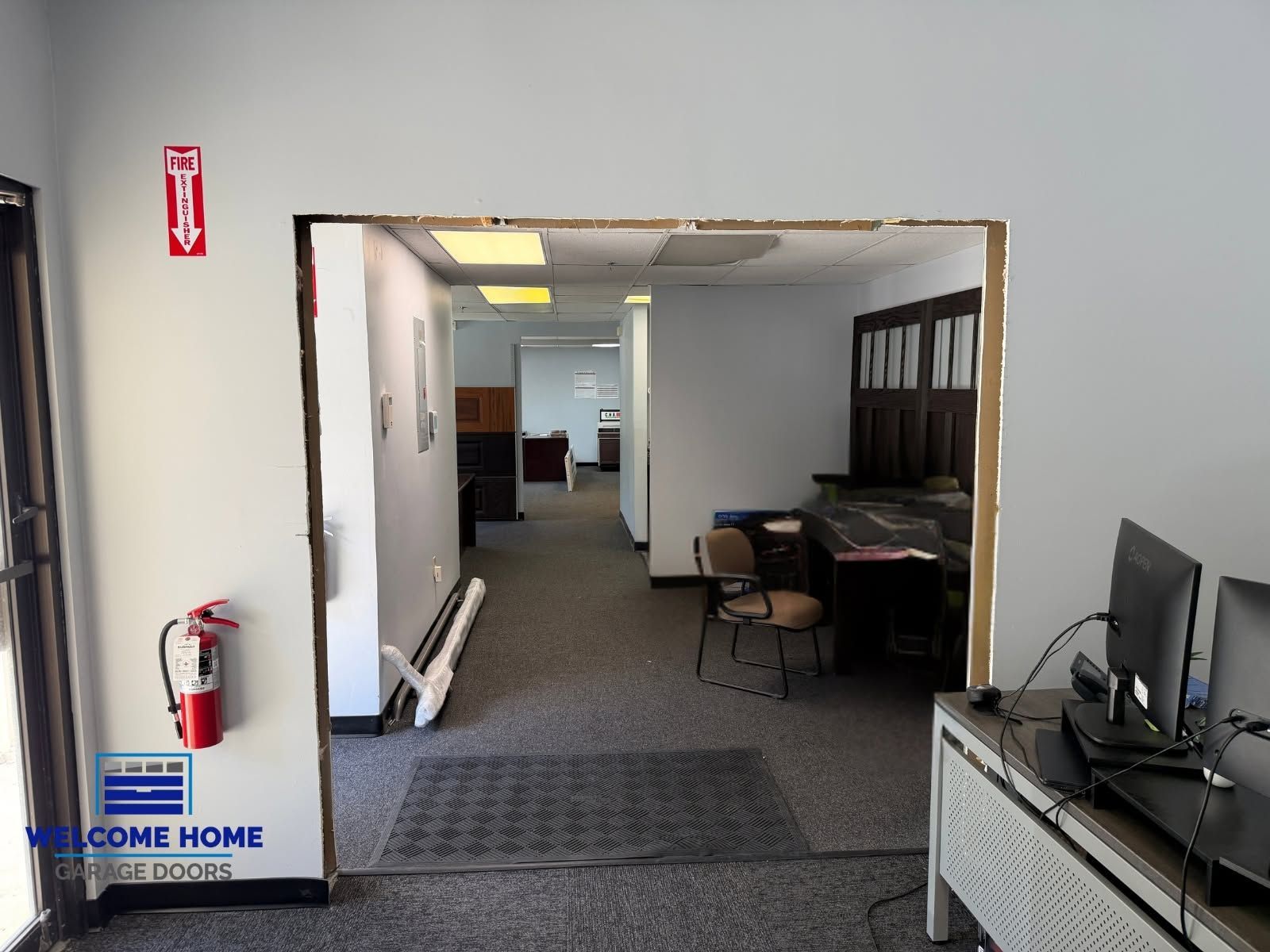Office hallway with desks, computers, and a fire extinguisher near the entrance.