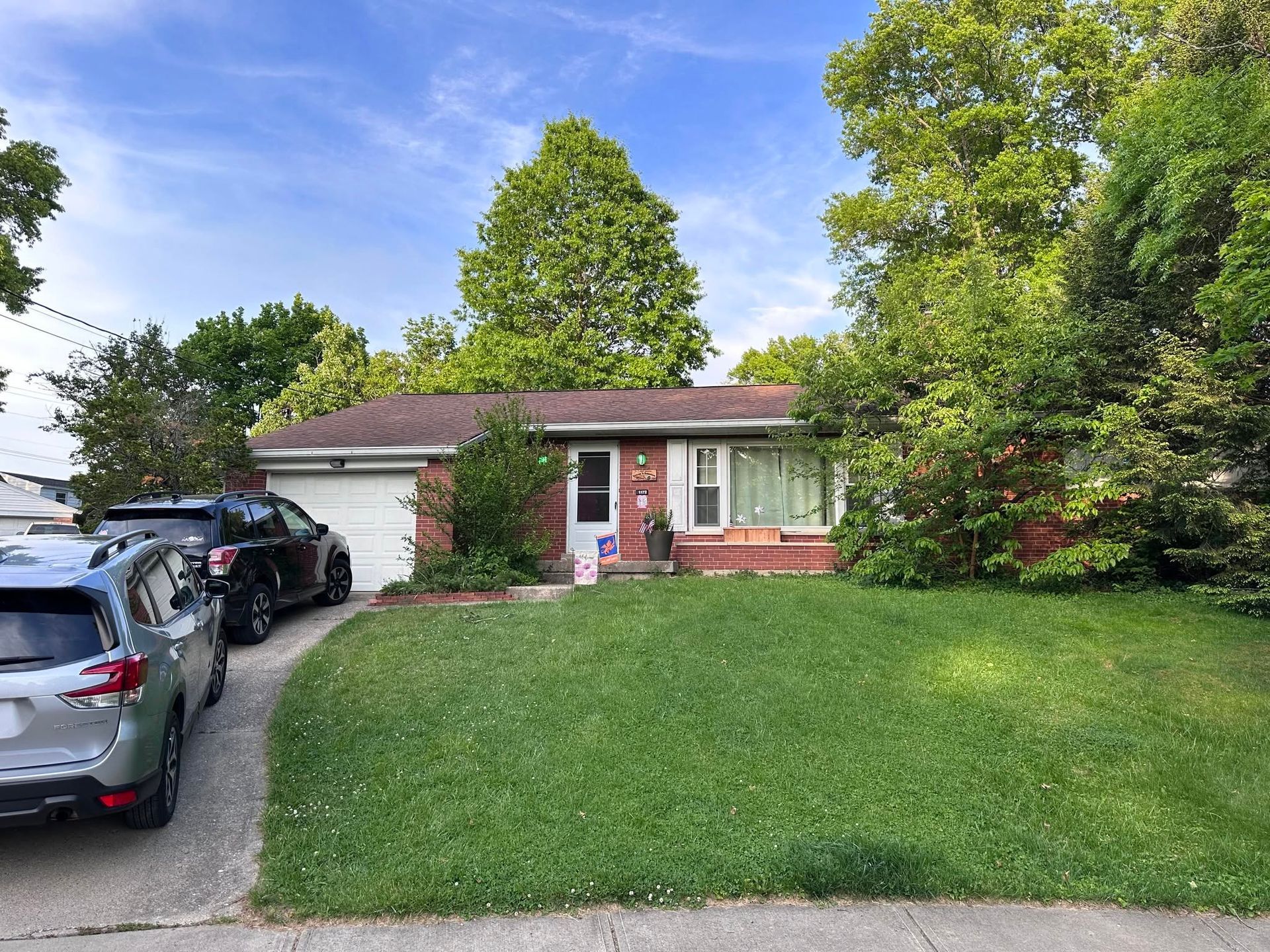 Single-story suburban house with red roof, green lawn, and cars parked in the driveway