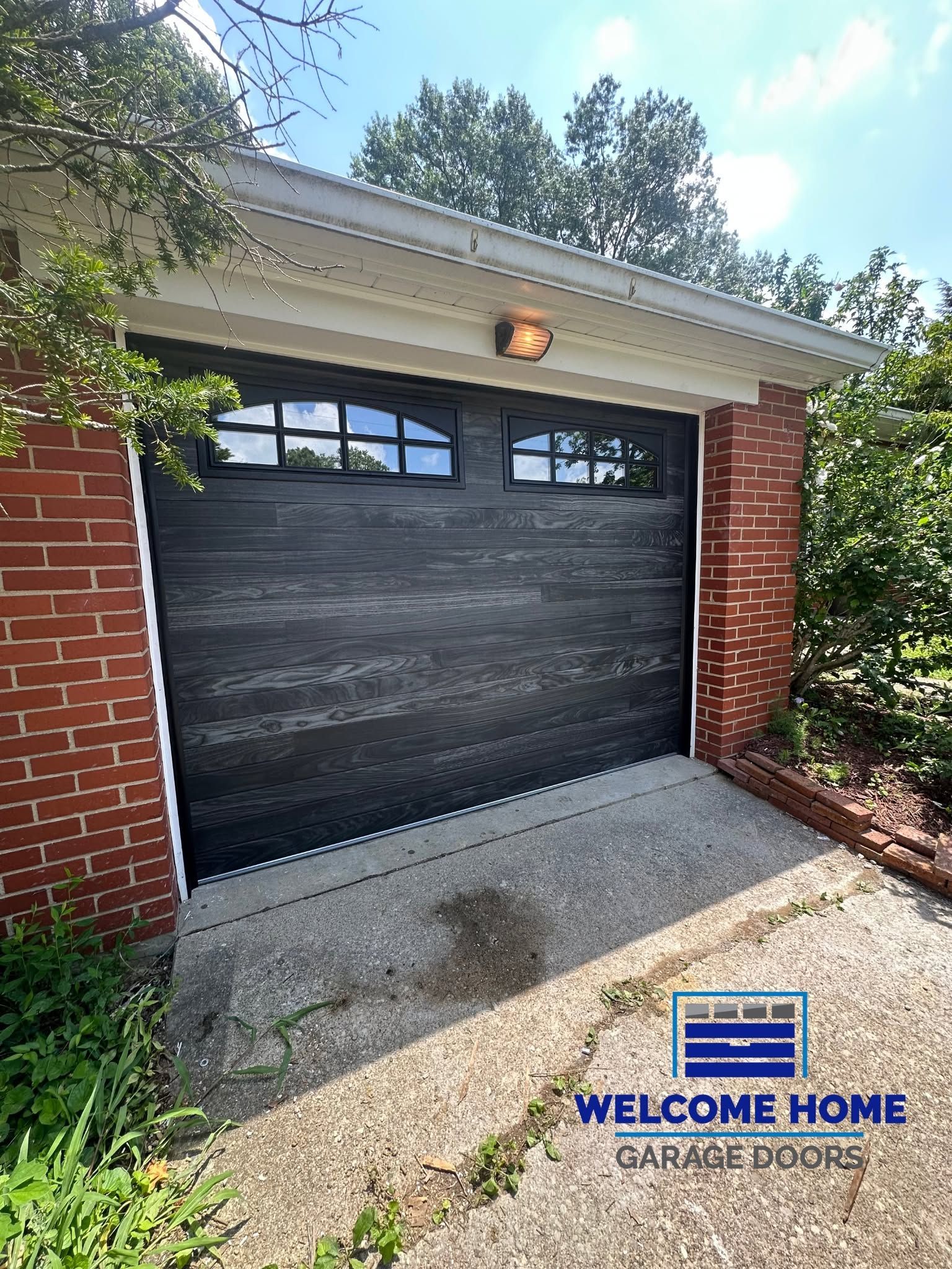 Home garage with black door, brick sides, and a welcome mat on the driveway