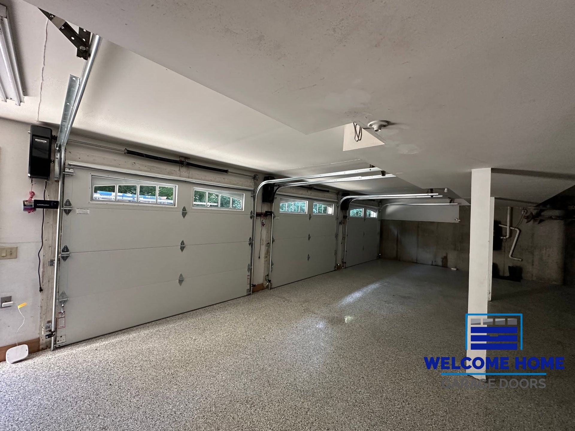 Spacious unfinished garage interior with white walls, gray floor, and closed garage doors